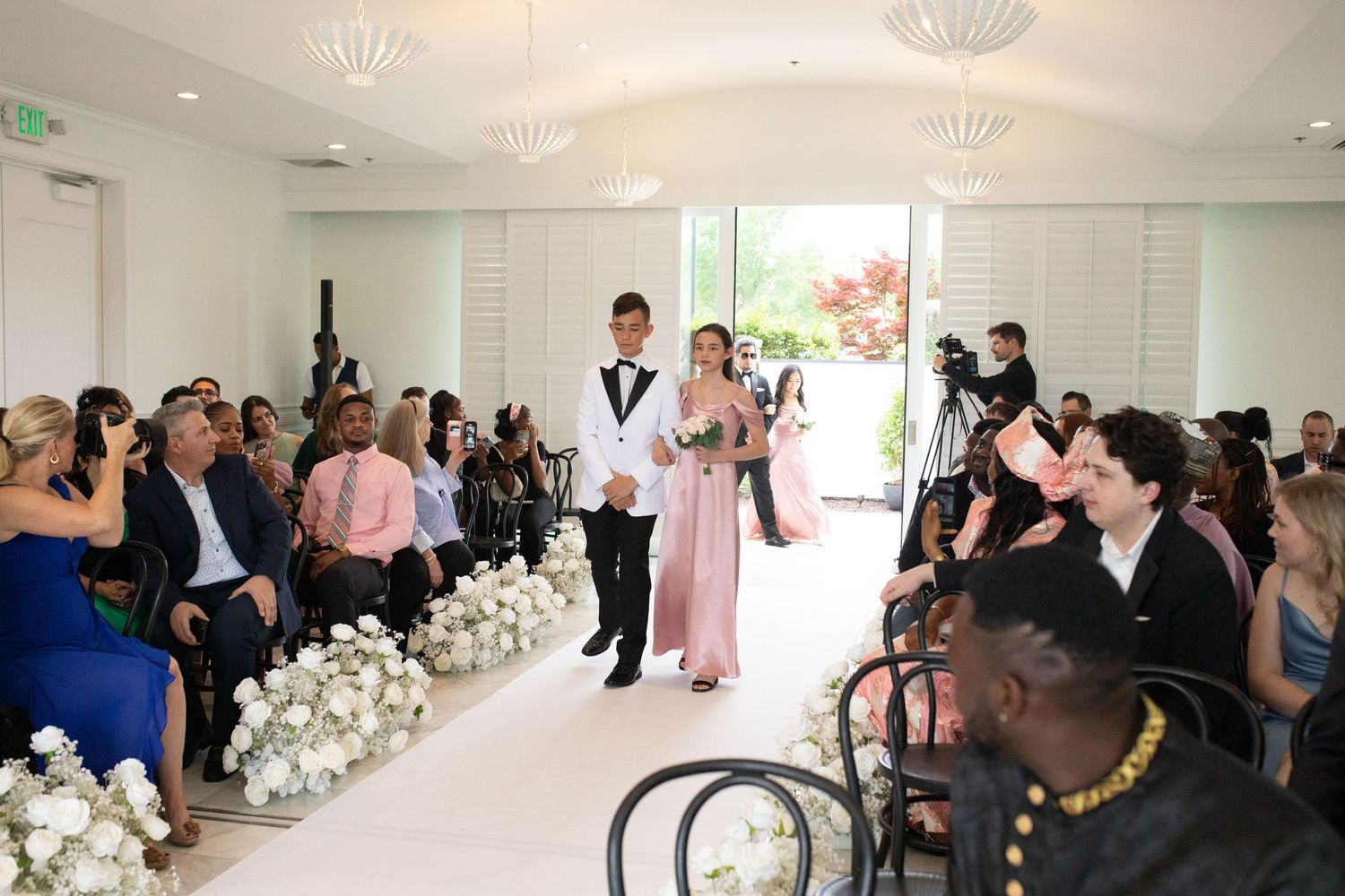 Wedding ceremony venue with white floral decorations and guests seated in an elegant indoor space.