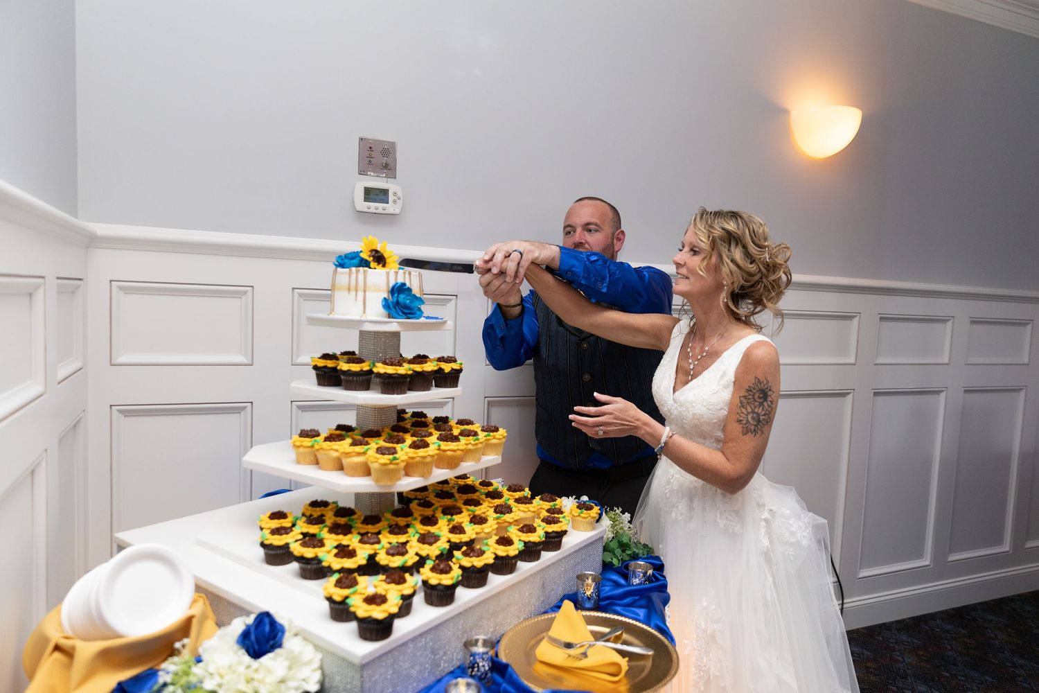 Bride and groom cutting a tiered cupcake tower with sunflowers at their wedding reception.