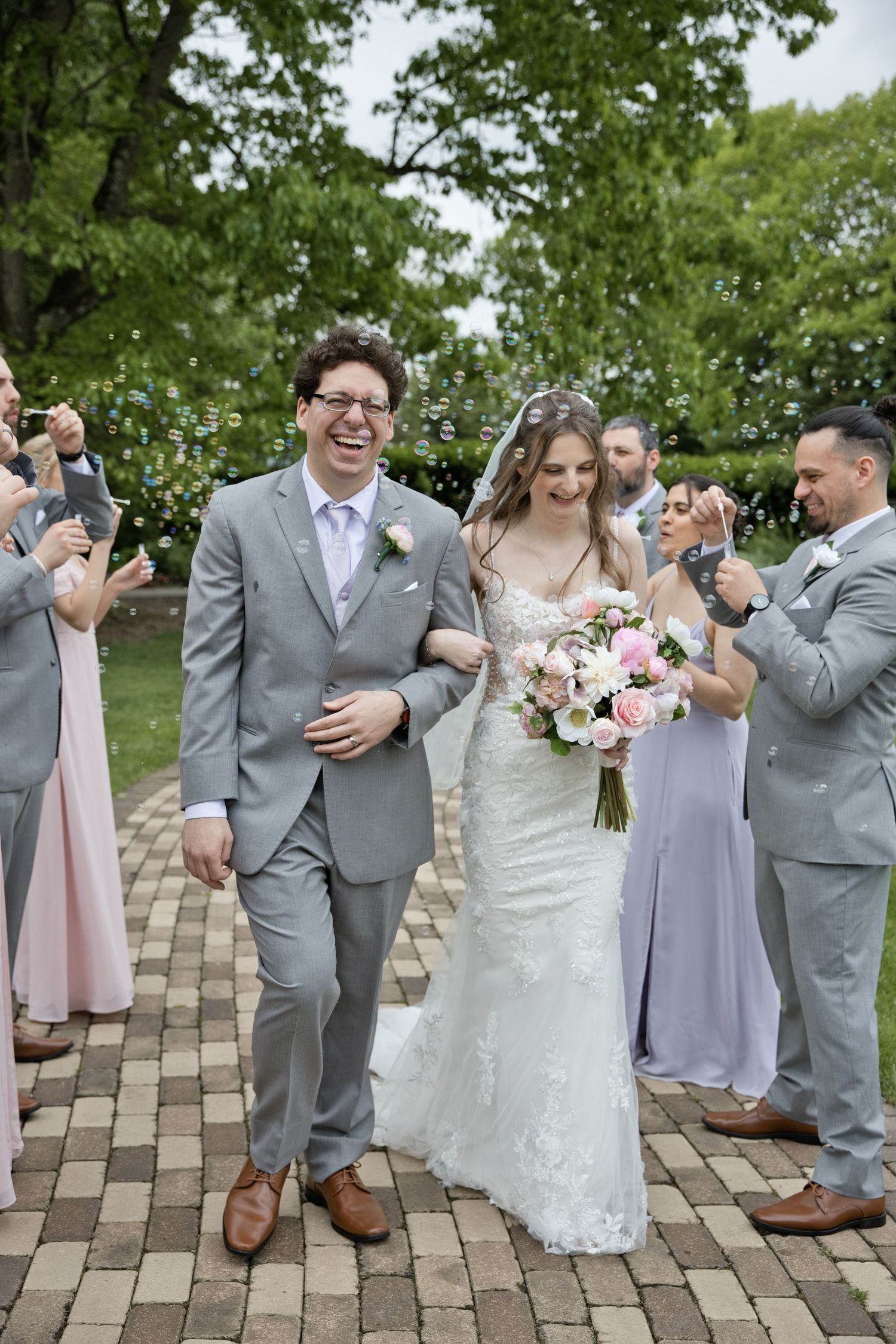 Joyful bride and groom walk together after wedding ceremony as guests blow bubbles outdoors.