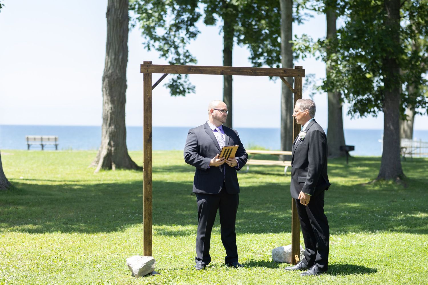 Outdoor wedding ceremony setup with wooden cross arch and waterfront view.