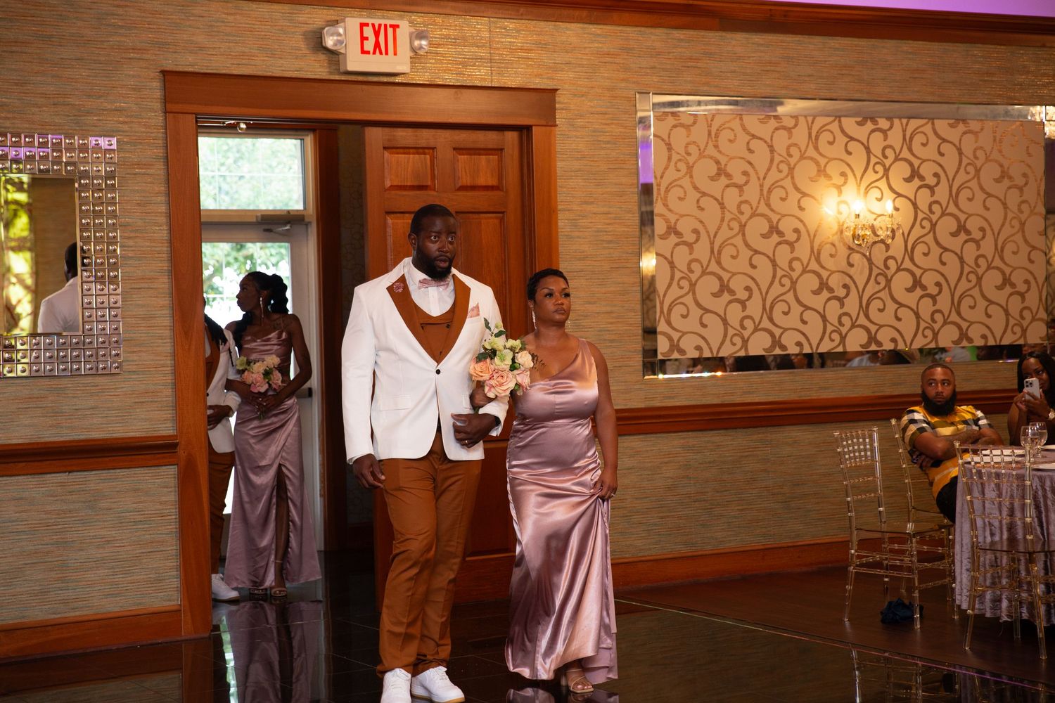 Dancers perform in an elegant banquet hall with wood-paneled walls and purple mood lighting.