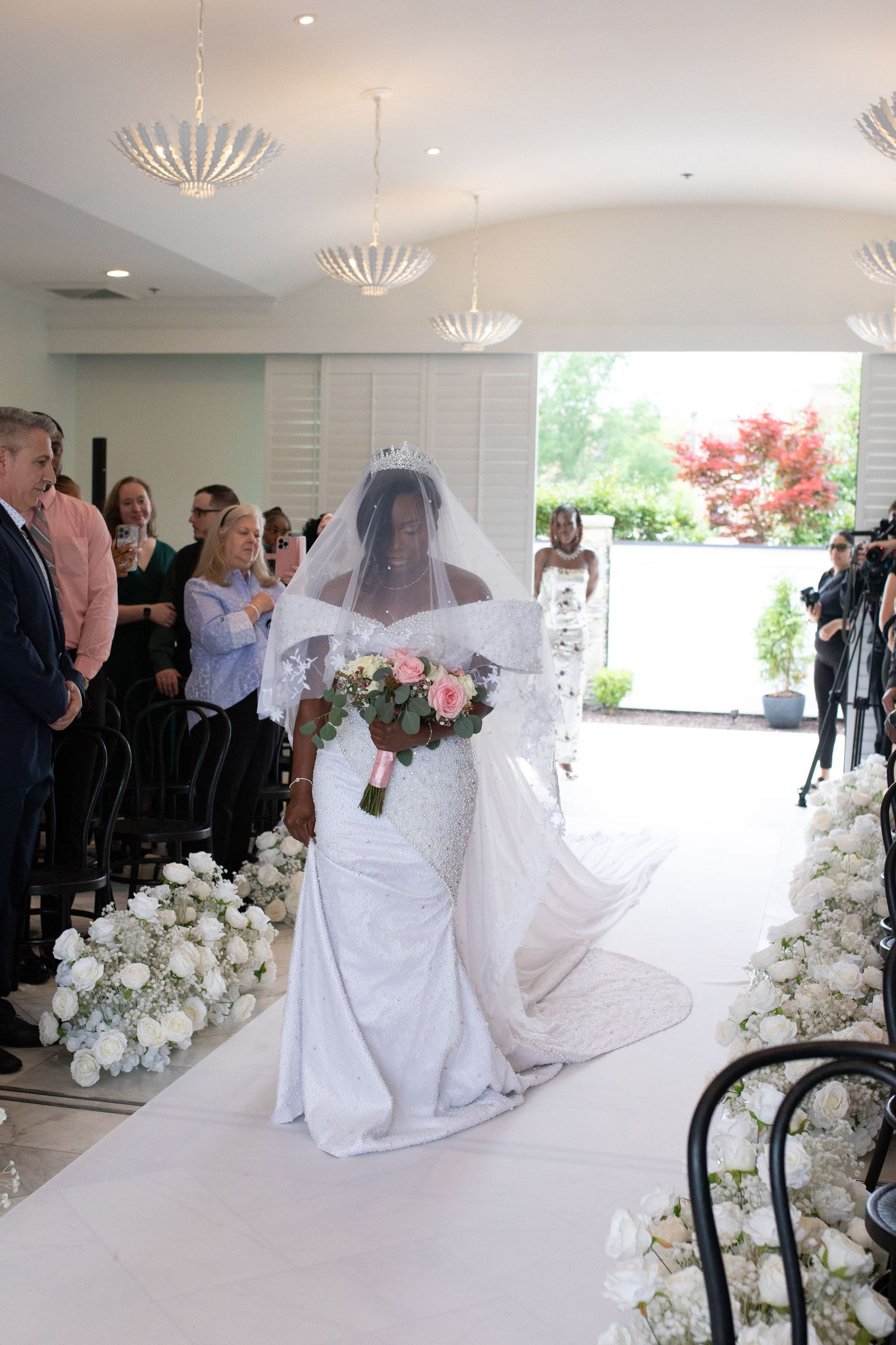 Wedding ceremony setup in an elegant white room with floral arrangements and chandeliers.
