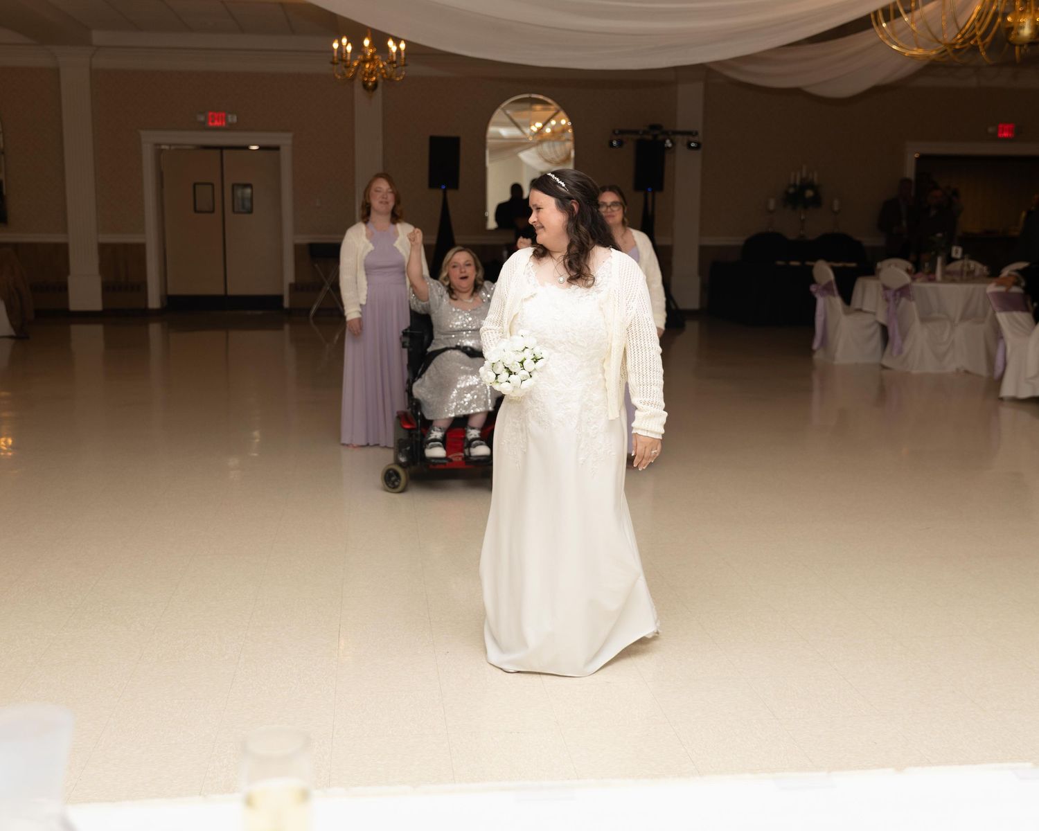 Bride in white gown walks across ballroom dance floor at elegant wedding reception venue.