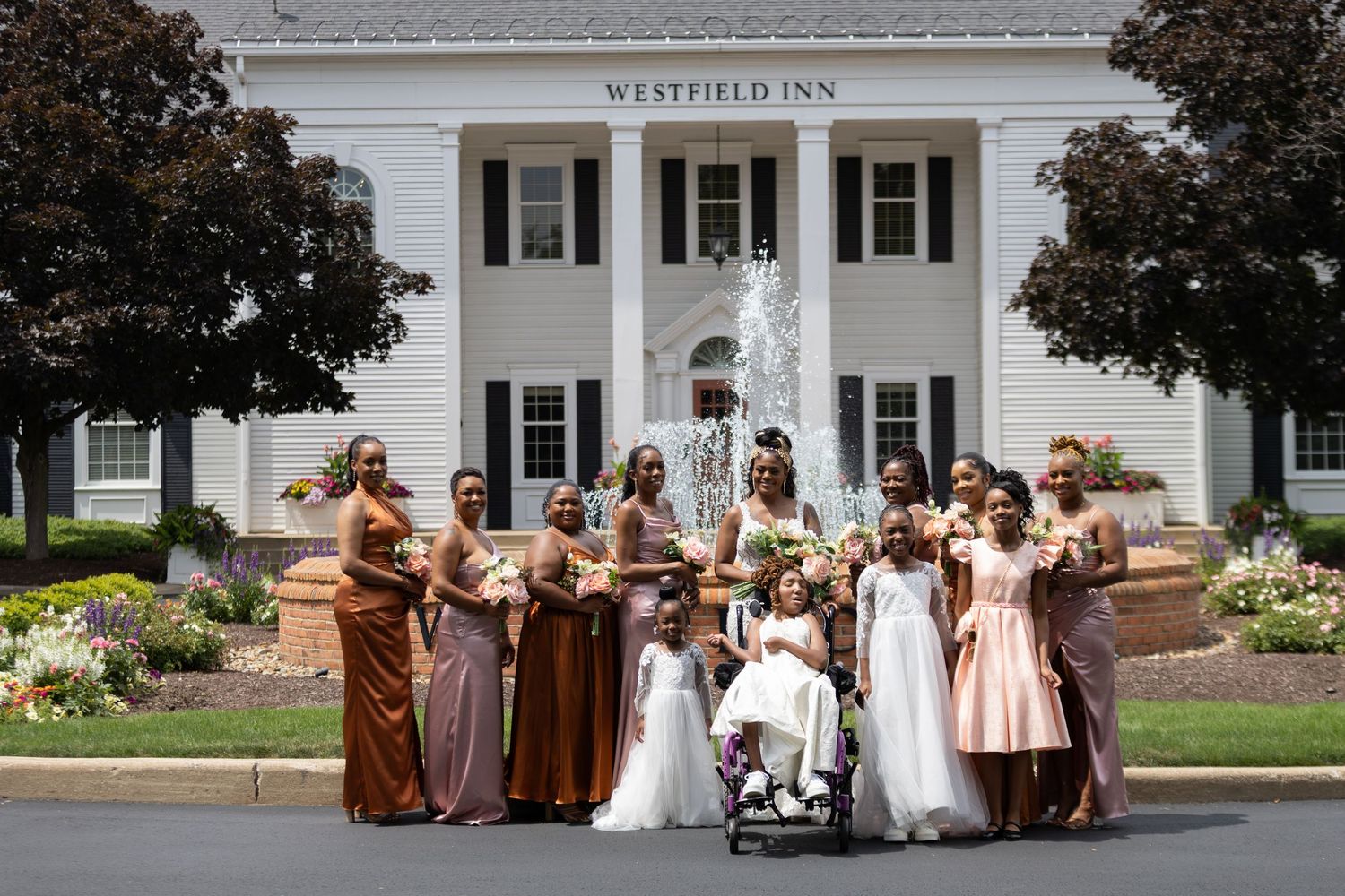 Wedding party in earth-toned dresses poses in front of Westfield Inn.