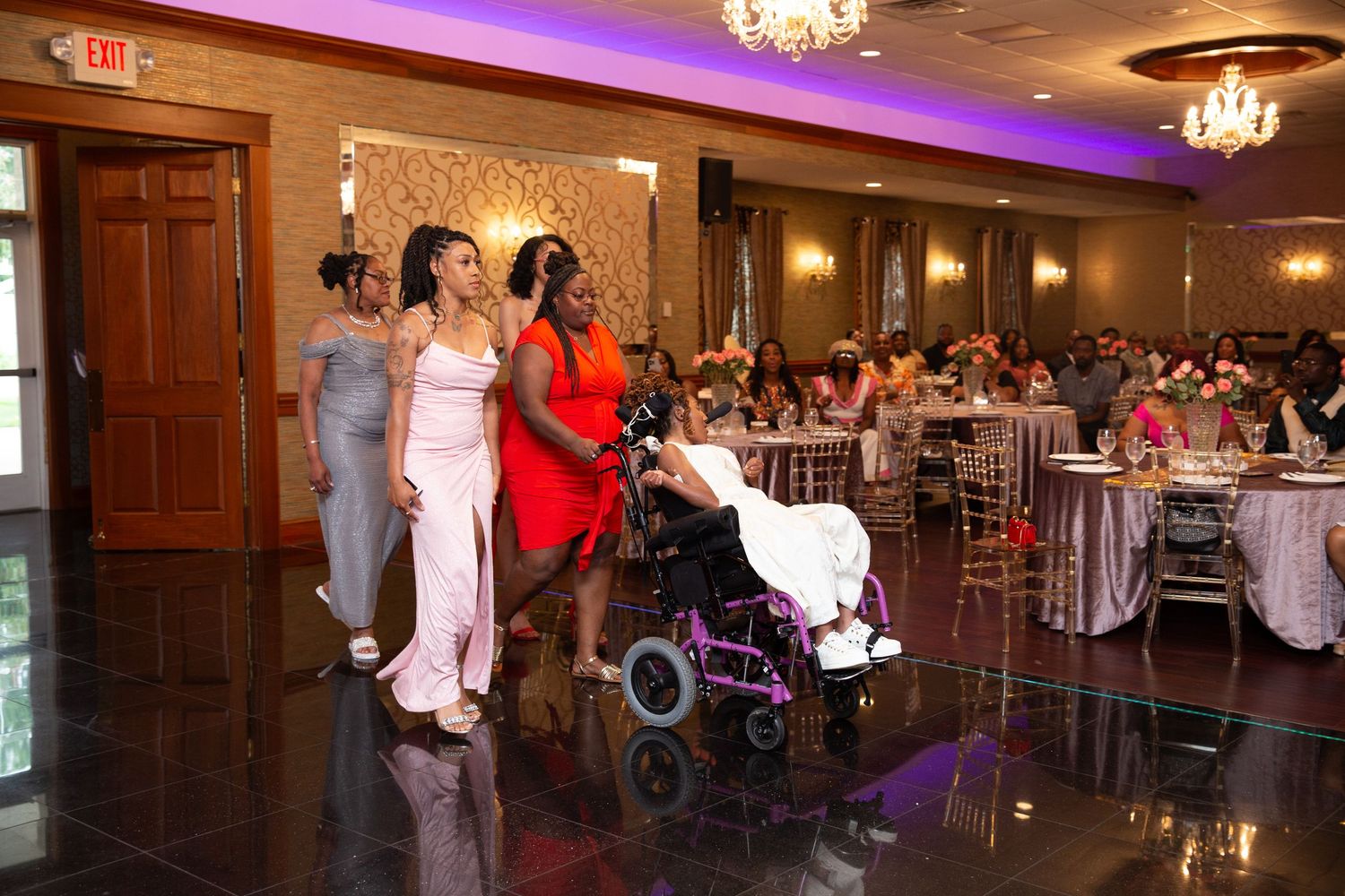 Wedding party dances and celebrates in an elegant ballroom with purple uplighting and chandeliers.