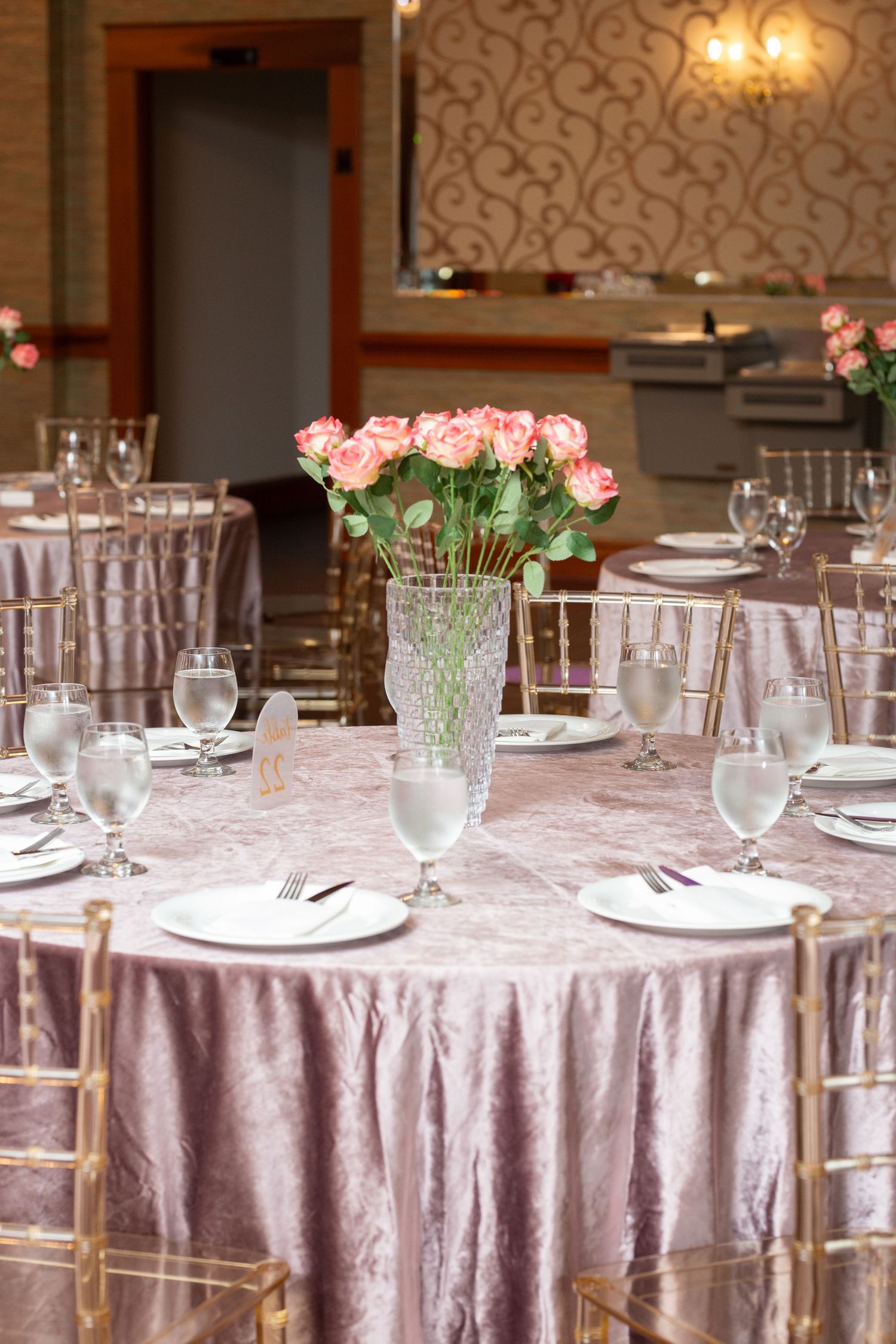 Elegant wedding reception tables with pink floral centerpieces and lavender tablecloths in a formal dining room.