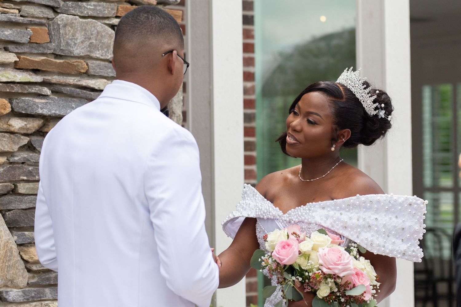 A joyful wedding moment captured outside against a stone wall backdrop with pink floral bouquet details.