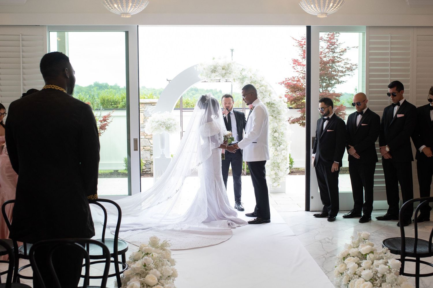 Wedding ceremony in progress in a bright modern venue with white floral decorations.