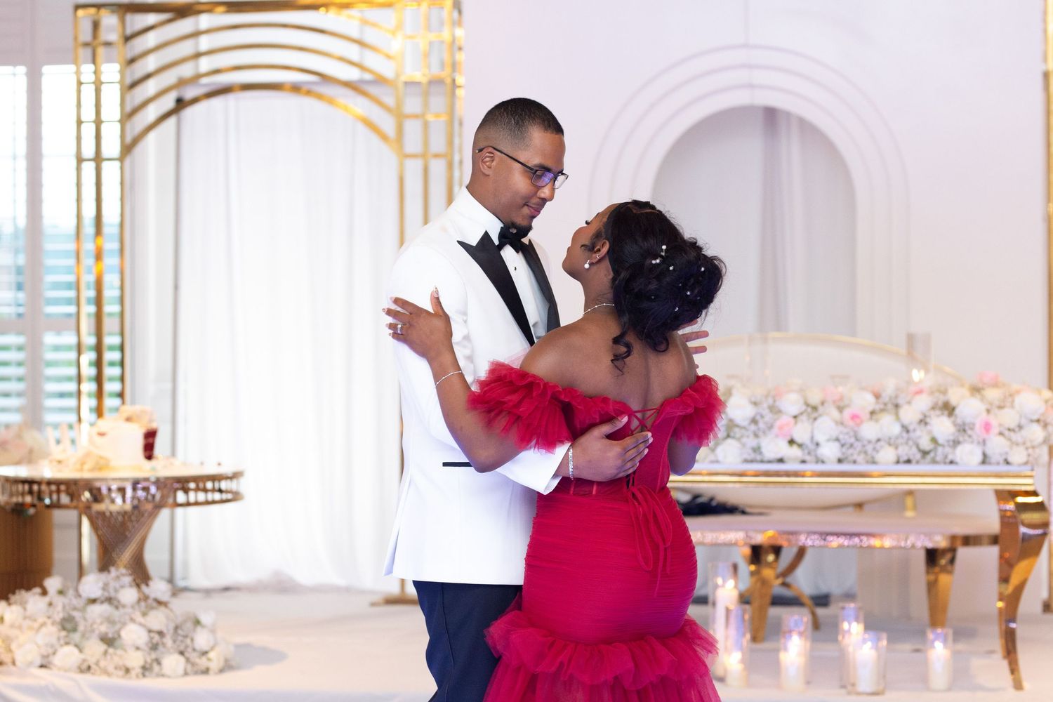 Couple dancing together in white tuxedo and red gown at their wedding reception.