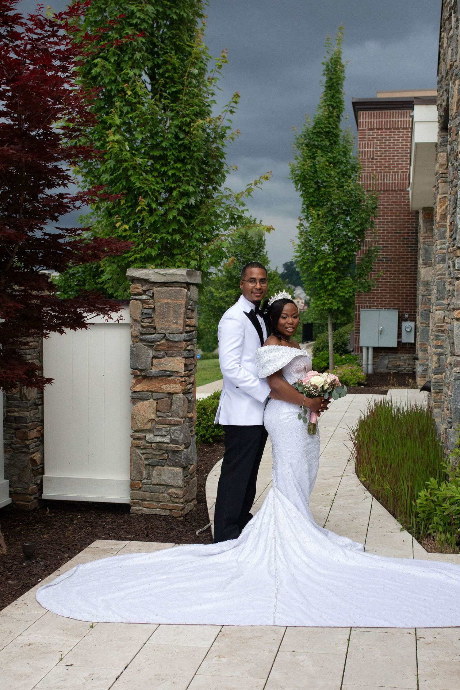 Bride and groom posing outdoors with flowing wedding dress train against stone architecture.