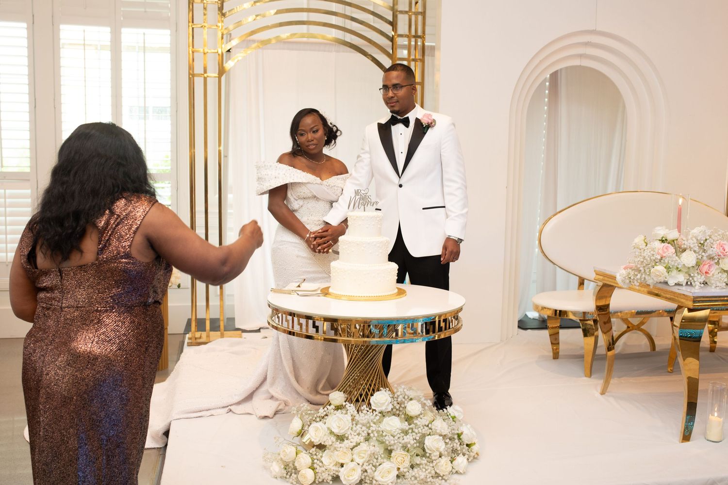 Wedding cake cutting moment captured in an elegant white and gold decorated venue.