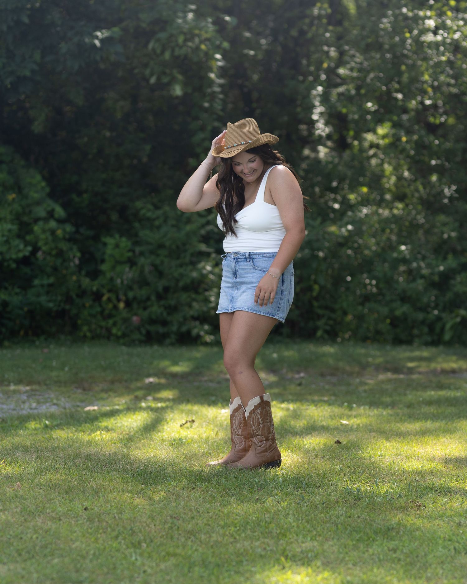 Country style pose in a shaded garden wearing cowboy boots and a straw hat.