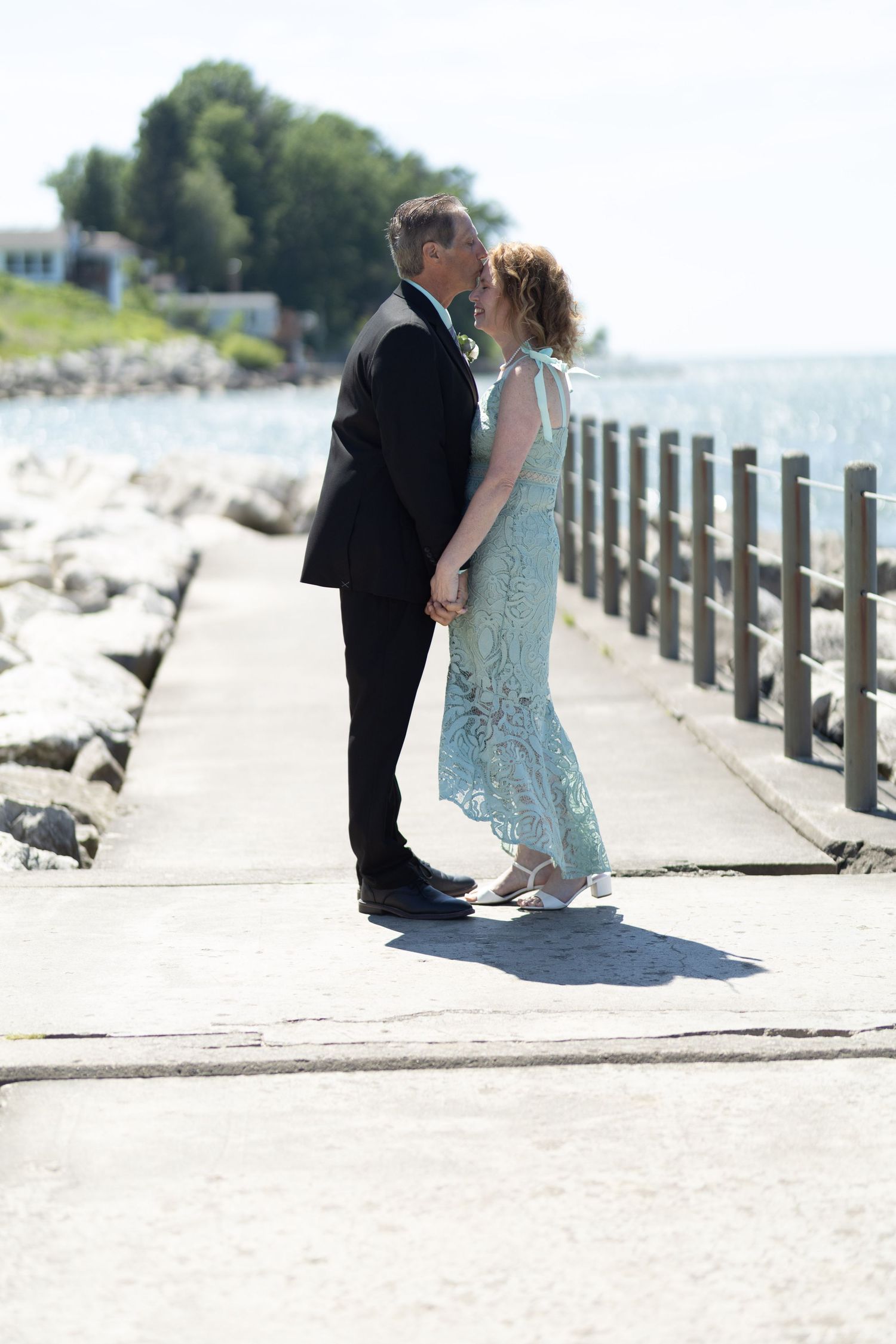 A romantic seaside scene with a couple in formal wear standing near a wooden railing.