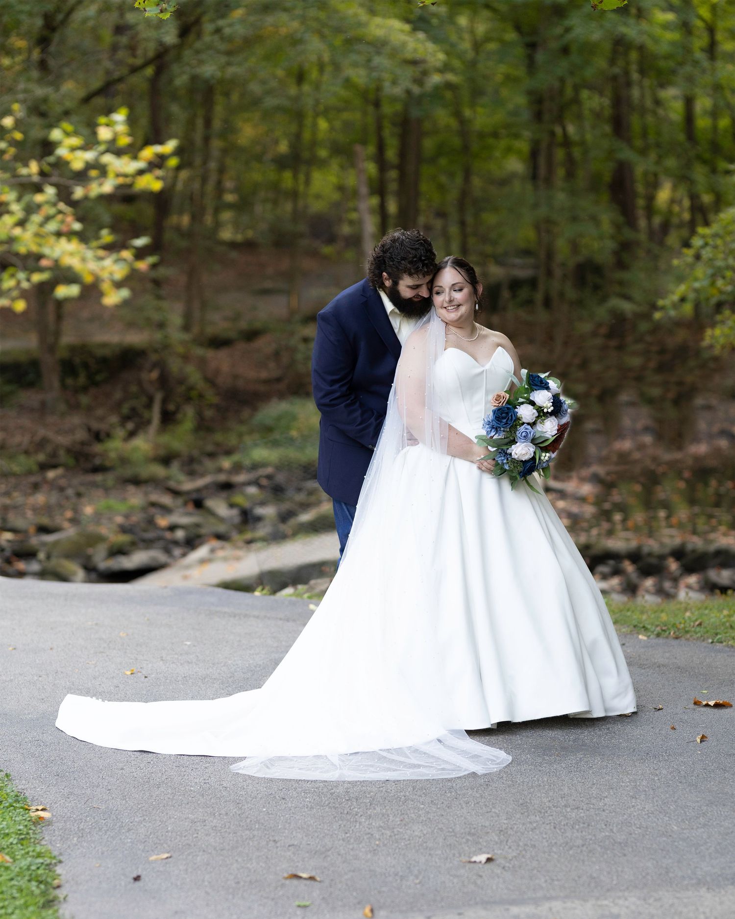 Elegant wedding couple poses on path with bride's dress train flowing behind.