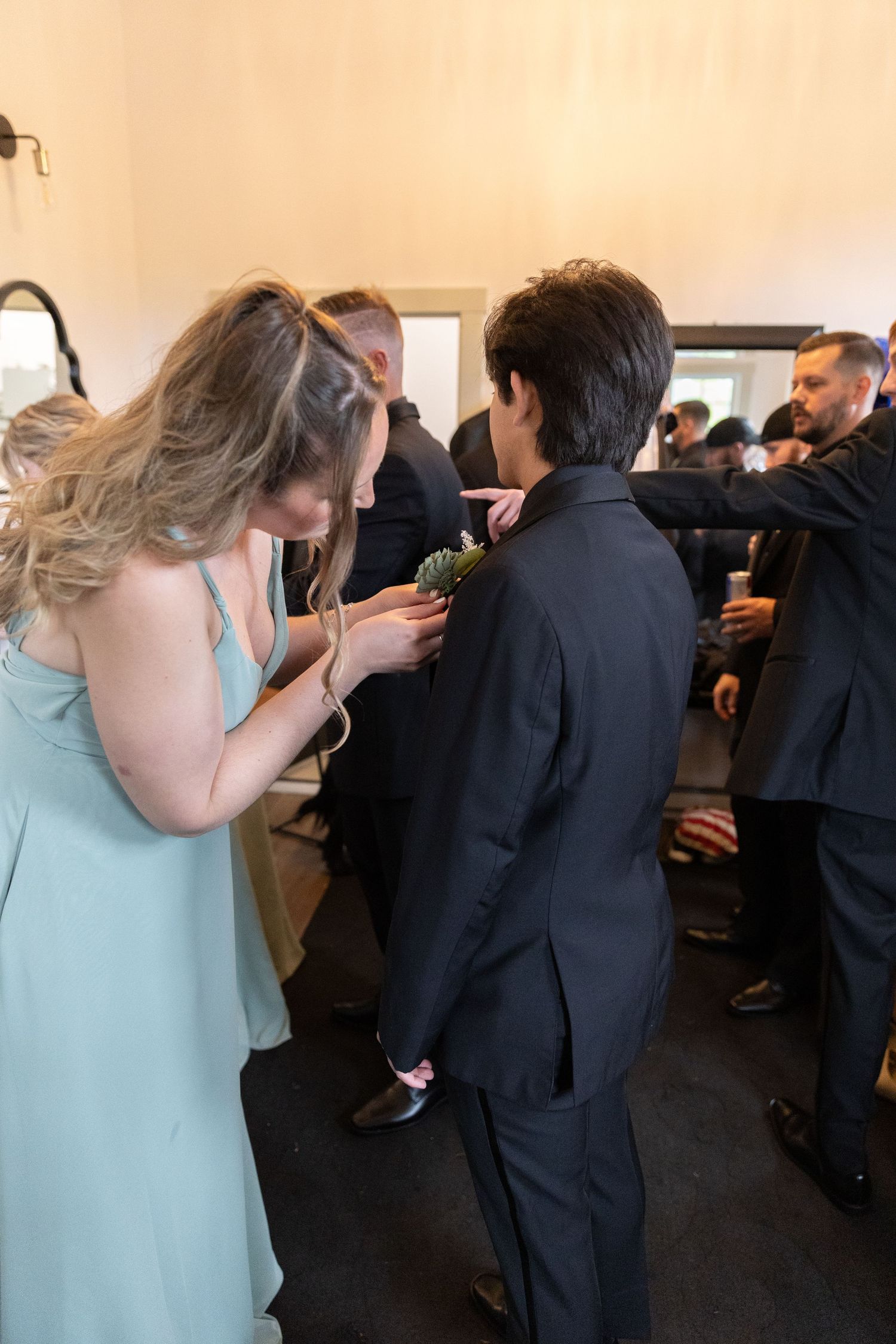 Woman in mint dress pinning boutonniere on young man in black suit at a wedding ceremony.
