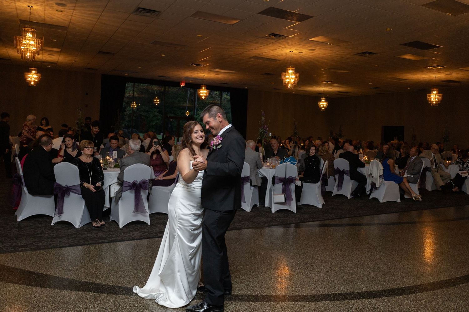 Large wedding reception hall with guests seated at round tables for dinner and dancing.