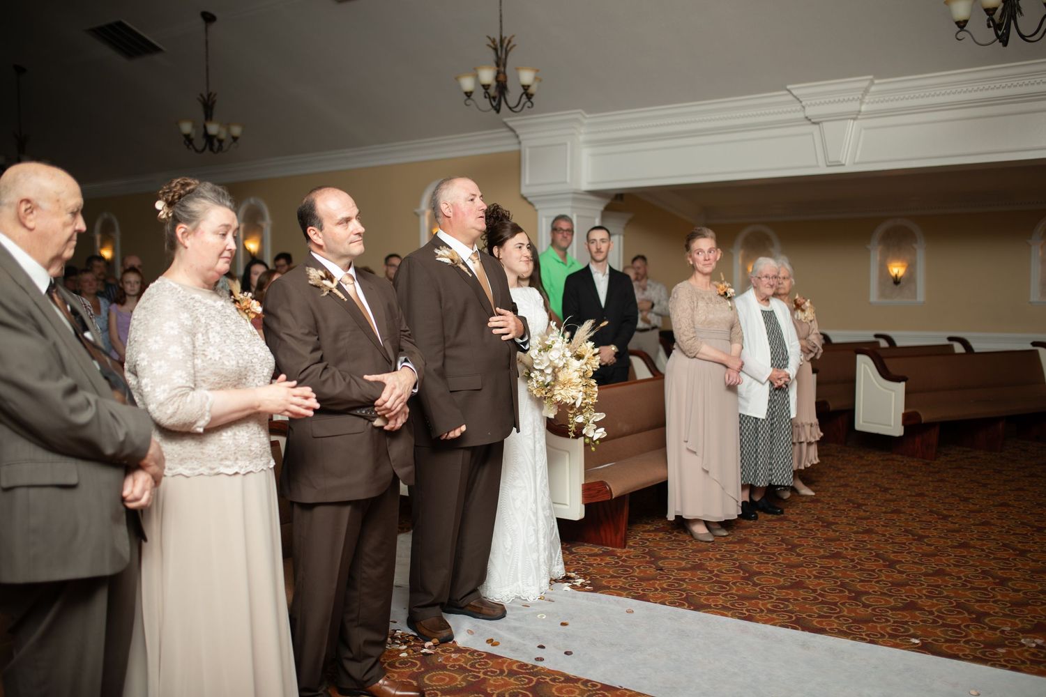 Wedding ceremony in progress with guests standing in an elegant venue with cream walls.