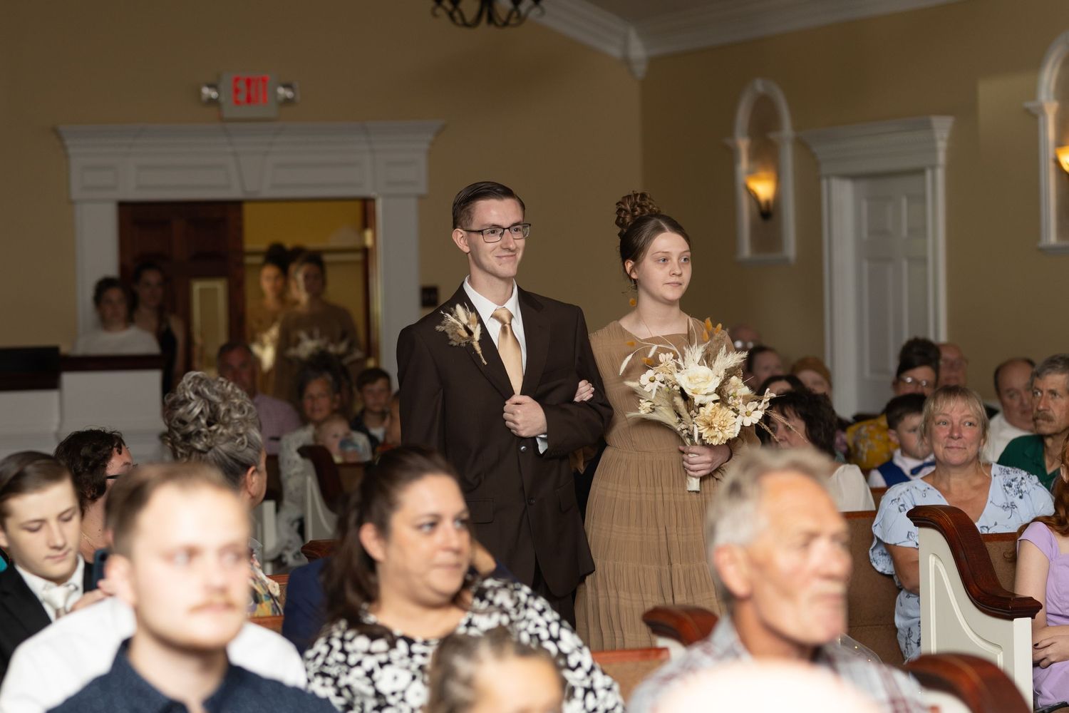 Wedding ceremony in progress with guests seated in an elegant hall with chandeliers.