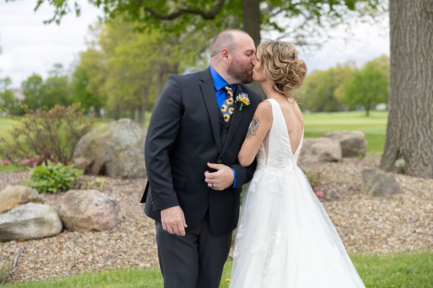 Bride and groom sharing a romantic kiss outdoors on their wedding day, surrounded by lush greenery and natural stone landscaping.