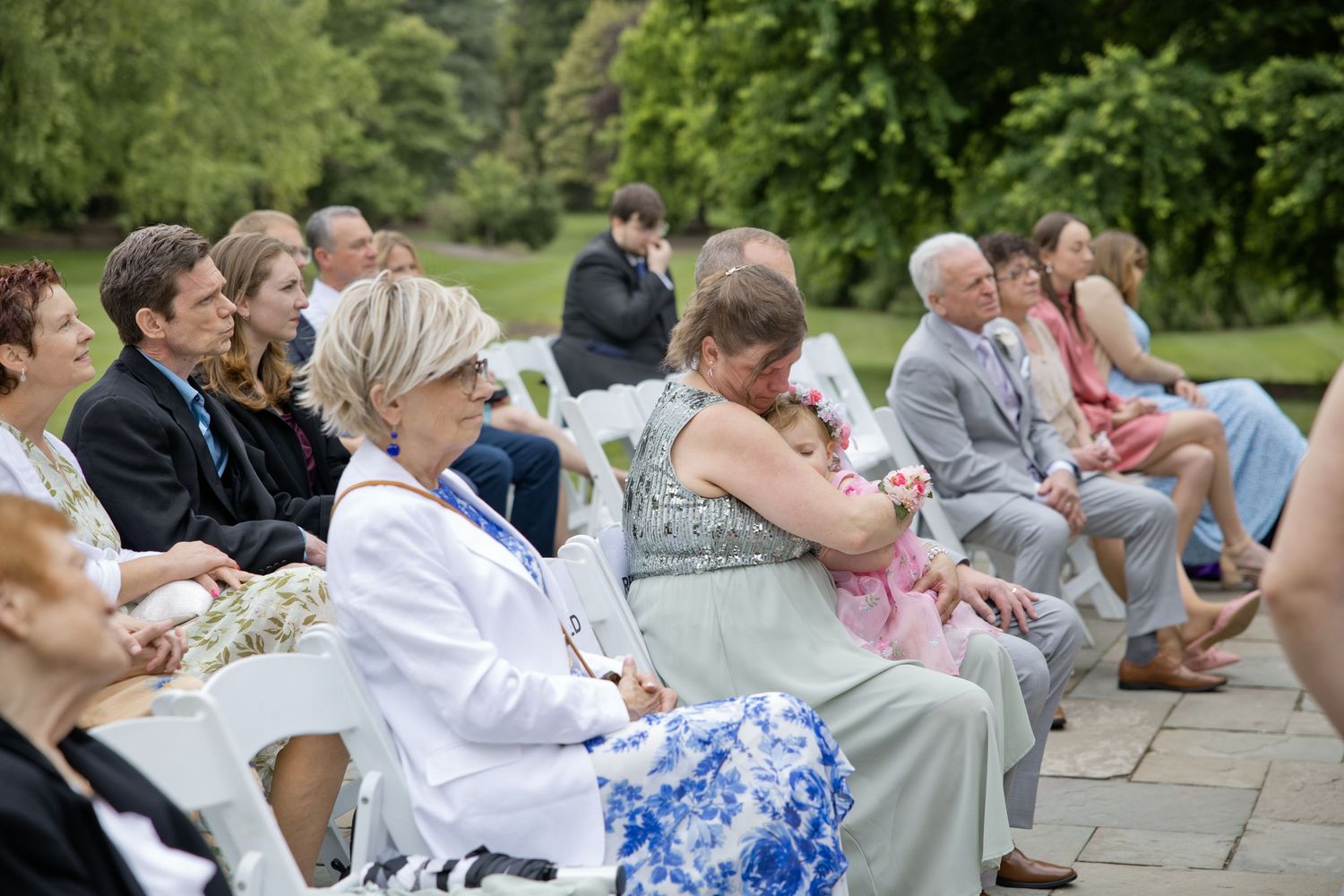 Guests seated outdoors at an elegant garden wedding ceremony on a stone patio surrounded by lush greenery.