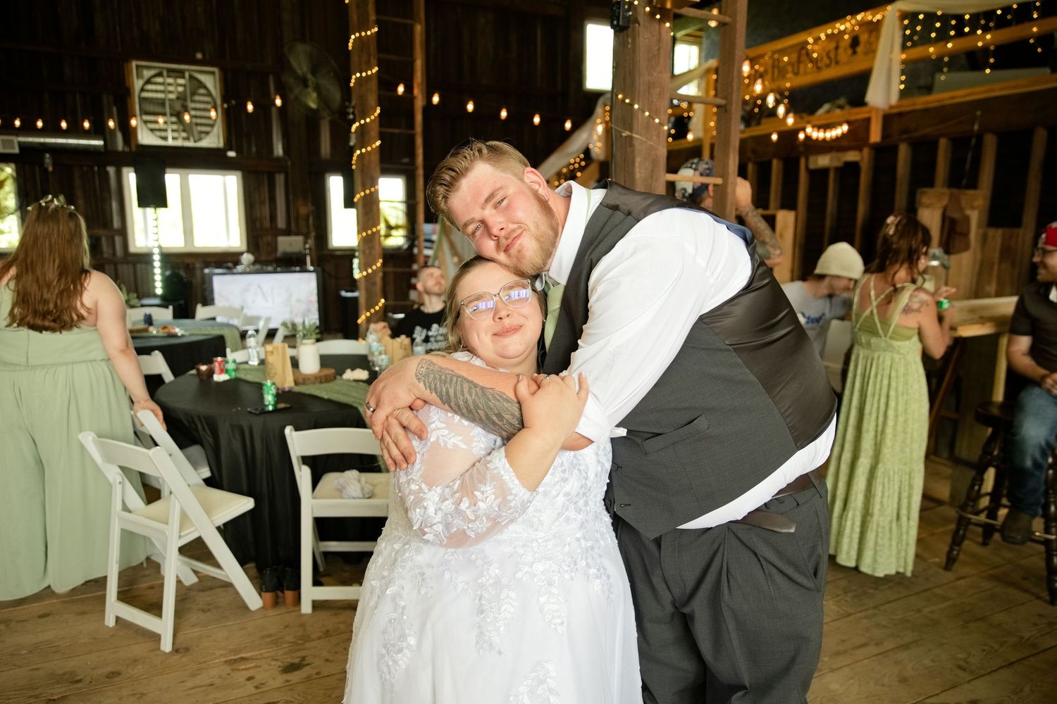 Happy couple embracing and smiling at a rustic barn wedding reception with string lights.