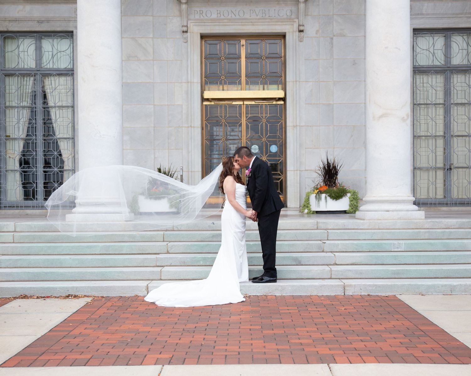 Elegant wedding scene at grand building with white columns and brick courtyard.