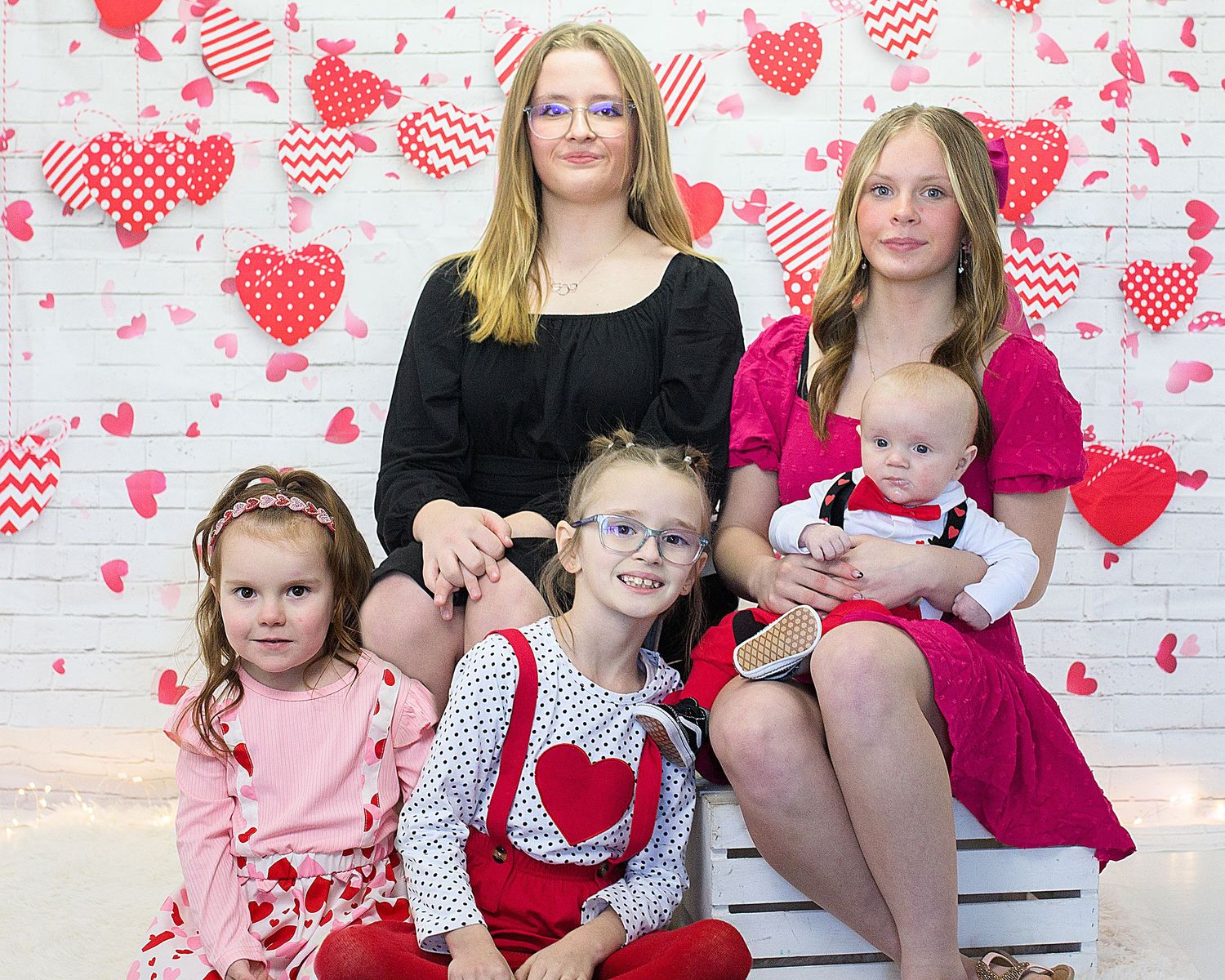 A family portrait against a Valentine's Day themed backdrop with heart decorations.