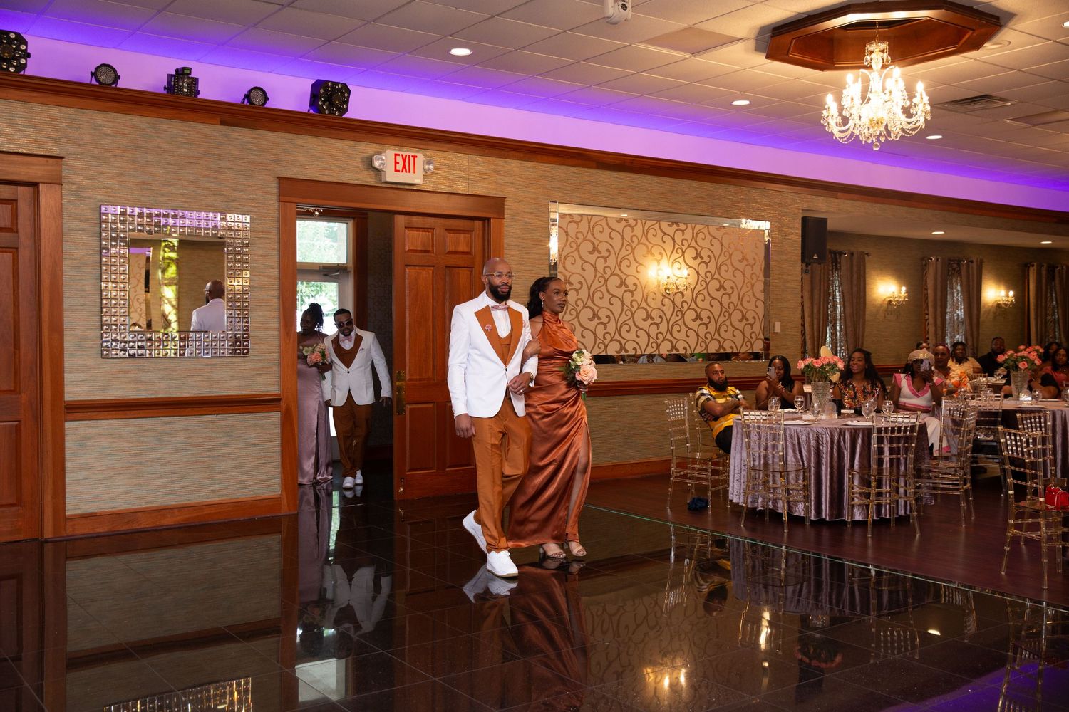 Elegant ballroom with purple uplighting and crystal chandeliers during a wedding reception.