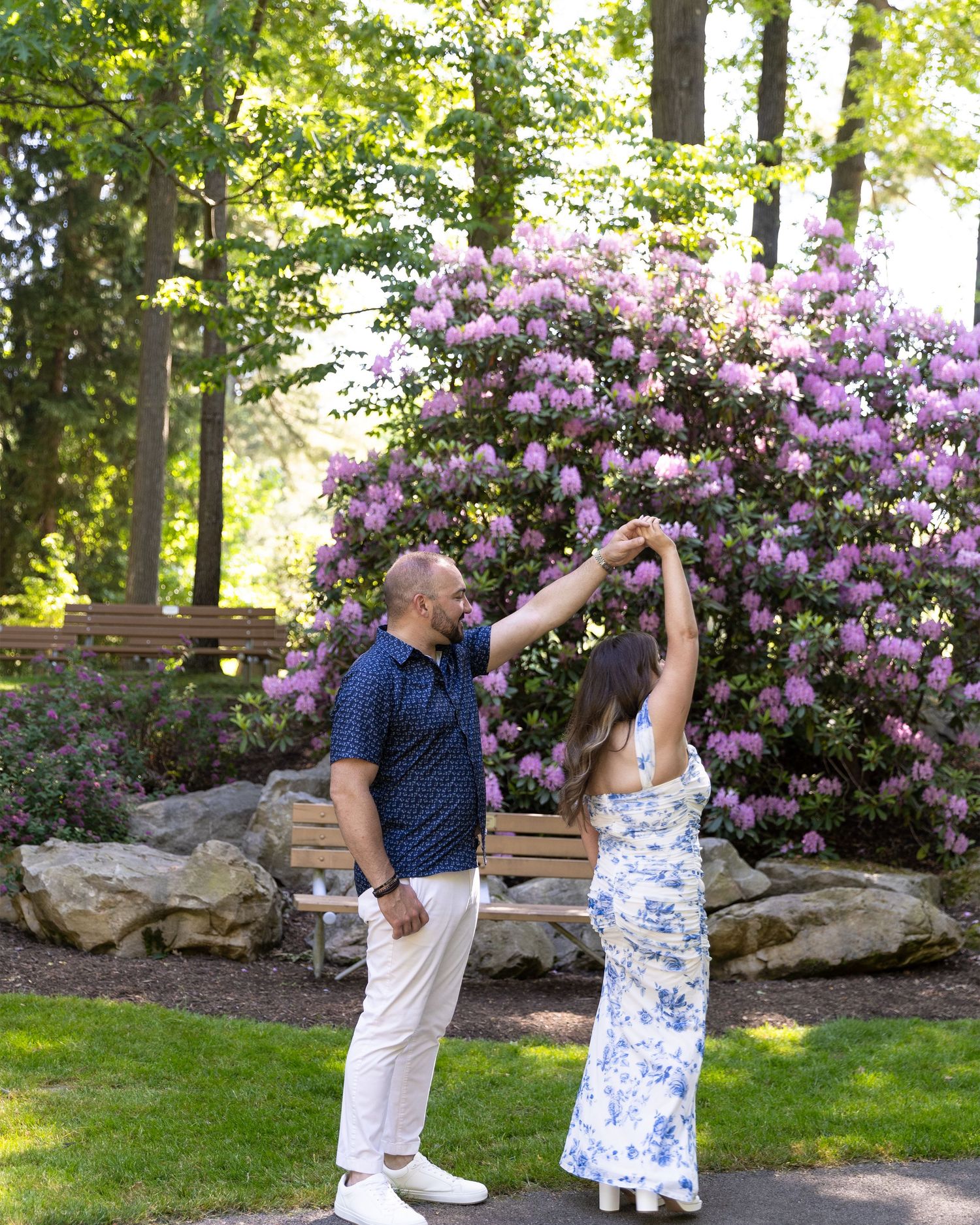 Couple dancing near blooming pink rhododendrons in a scenic garden park setting.