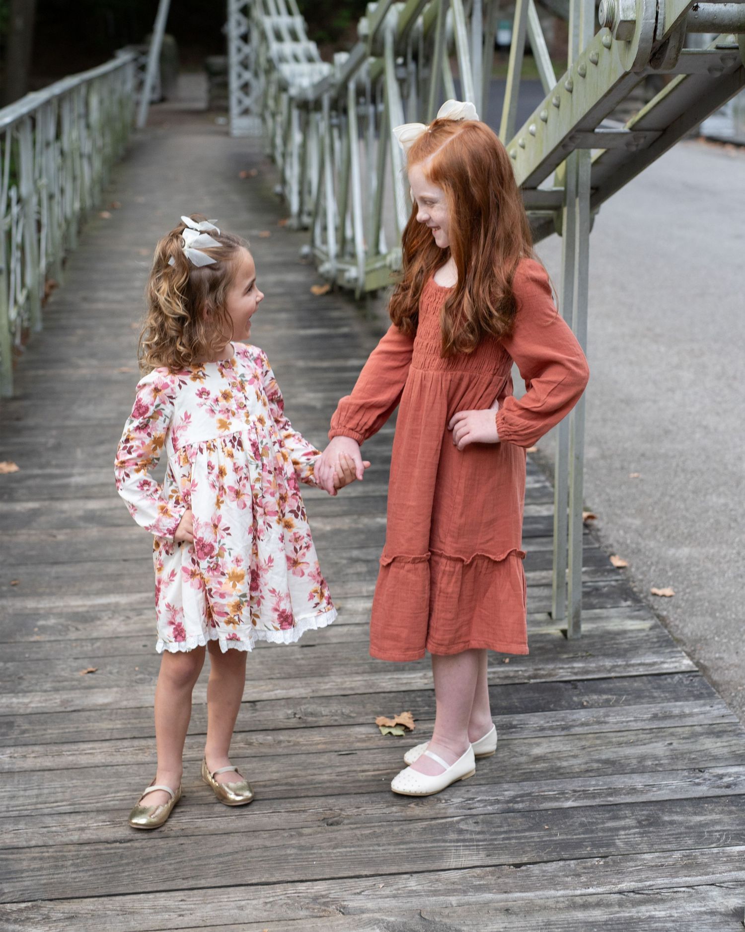 Two young children in floral and rust-colored dresses play together on a wooden boardwalk.