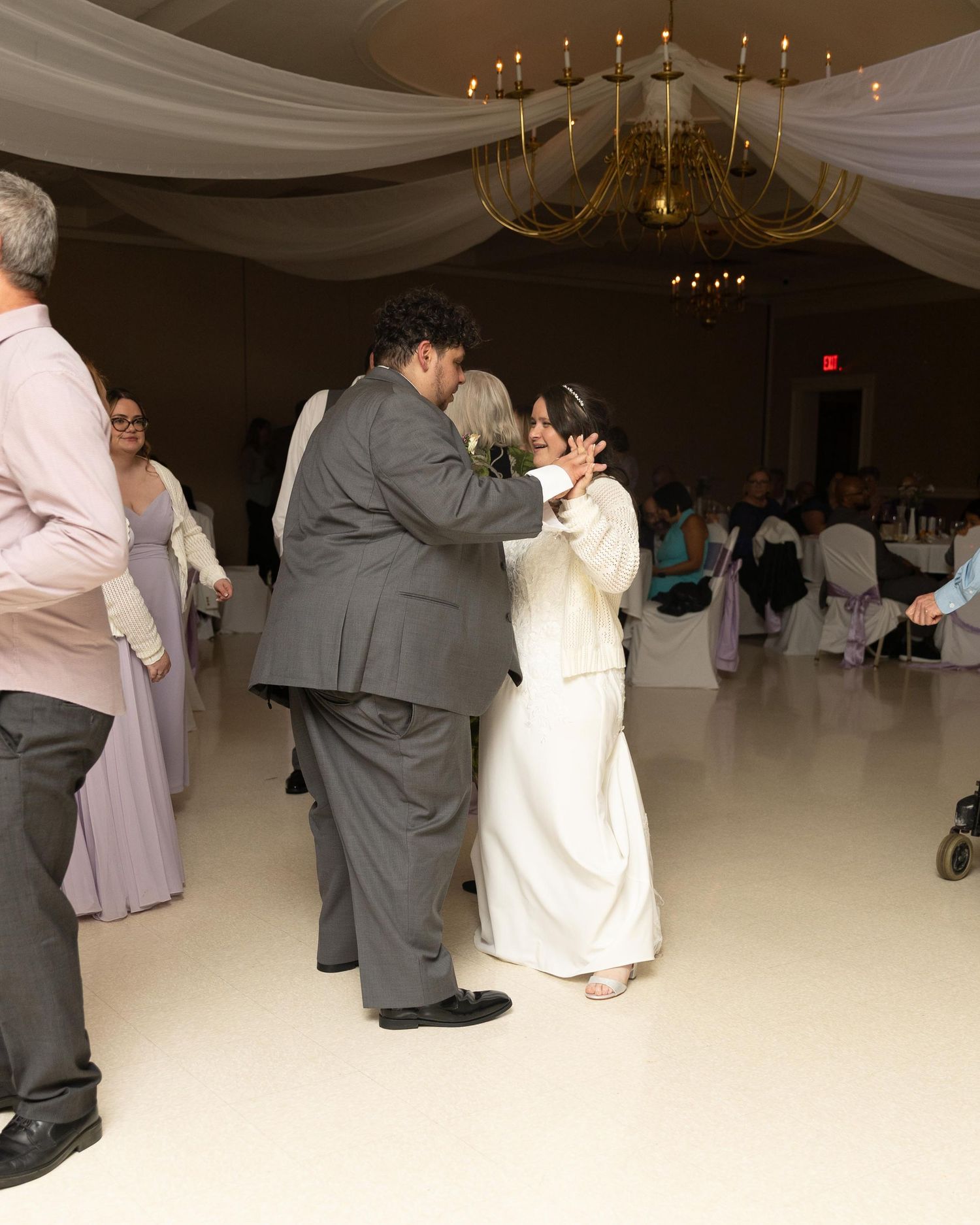 Bride and groom share their first dance at elegant wedding reception with chandelier and draped ceiling.