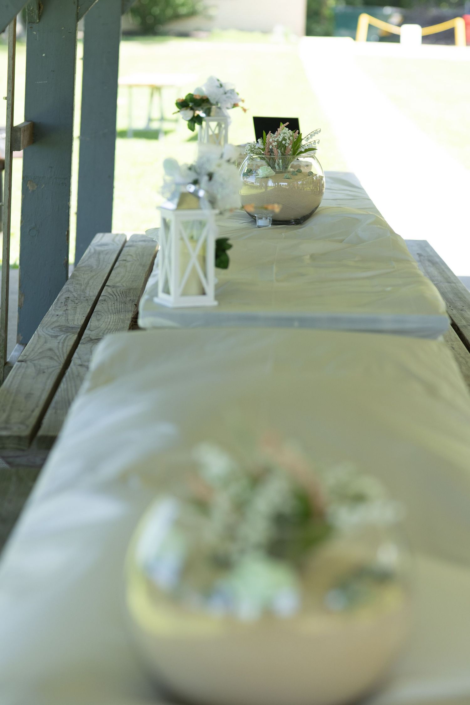 White tablecloth covered table with lanterns and floral centerpieces for wedding reception.