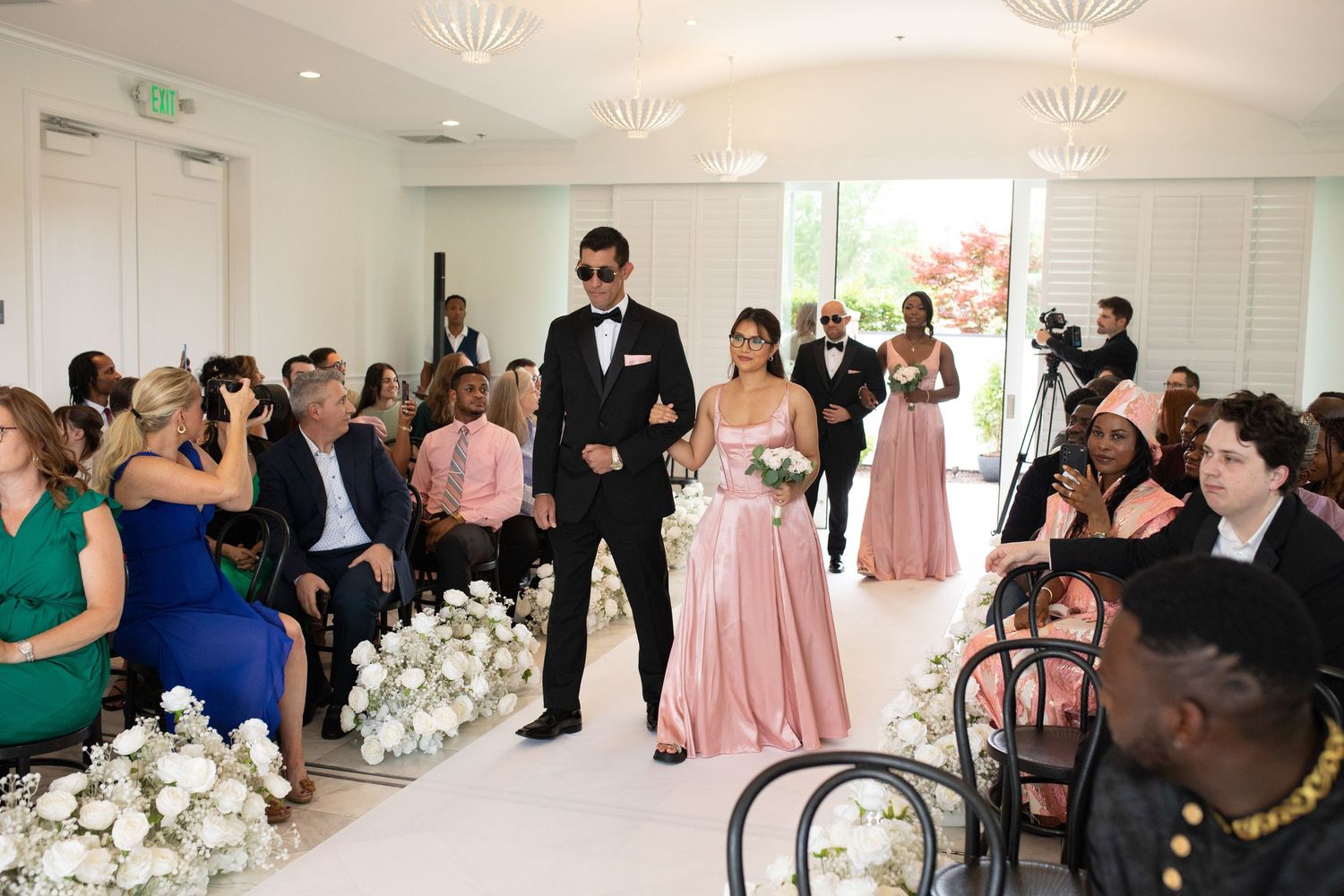 Modern wedding venue interior with white floral decorations and guests in formal attire.