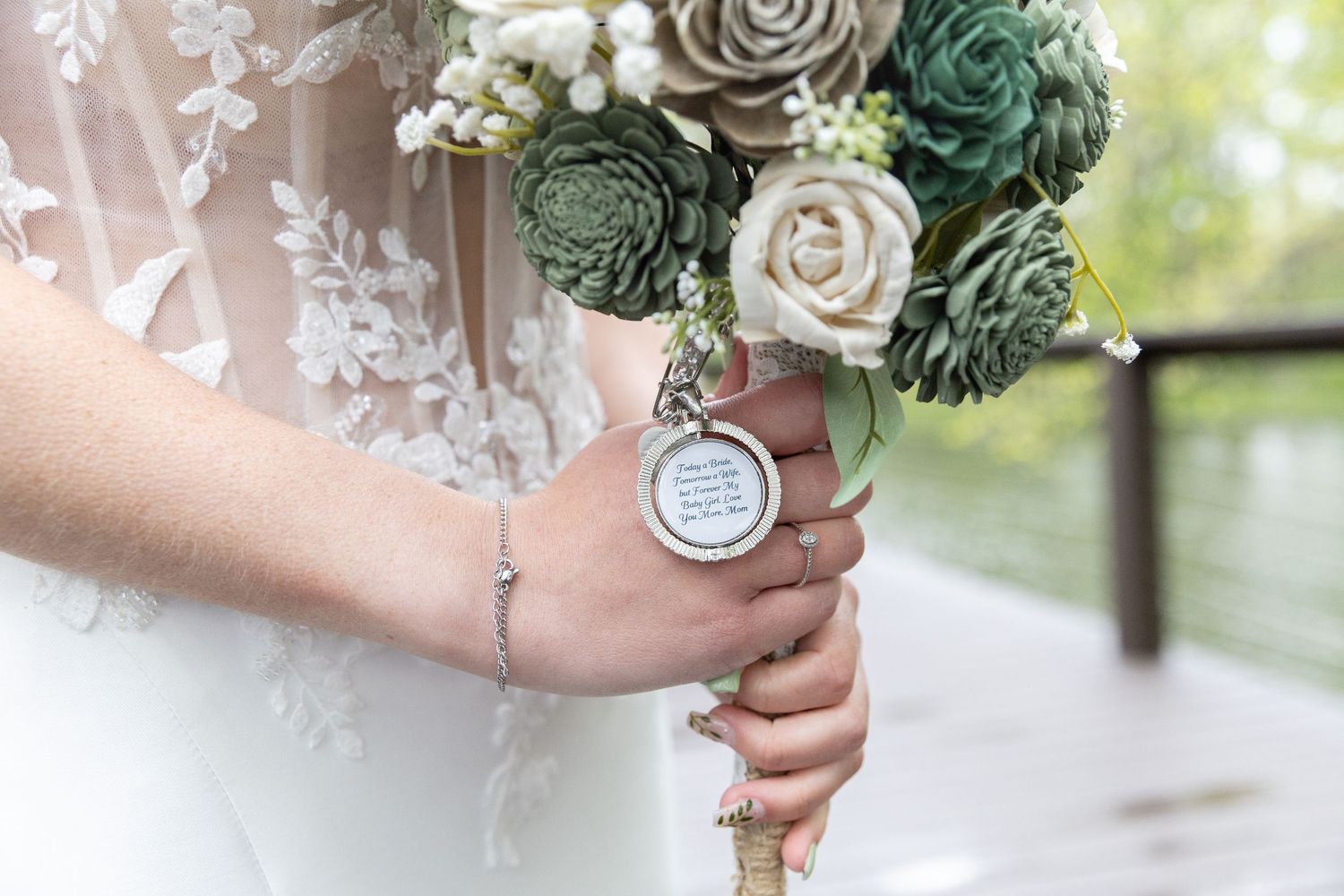 Bride holding a bouquet of silk flowers with a personalized round locket charm attached to the stems.