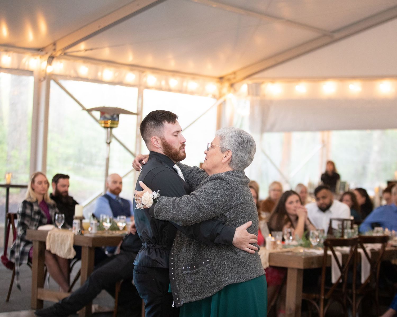 Groom shares emotional mother-son dance under string lights at elegant tented wedding reception.
