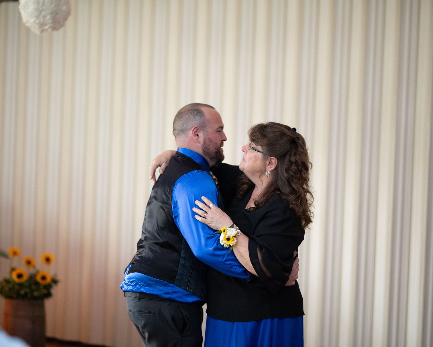 Couple sharing a romantic dance embrace at a wedding reception with sunflowers and striped wallpaper backdrop.