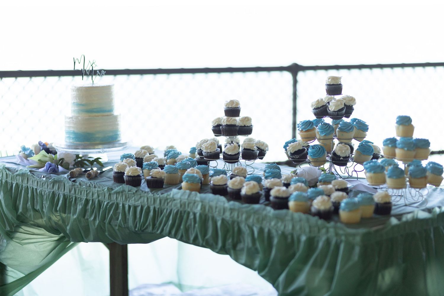 Wedding dessert table with blue and white cupcakes and tiered cake display.