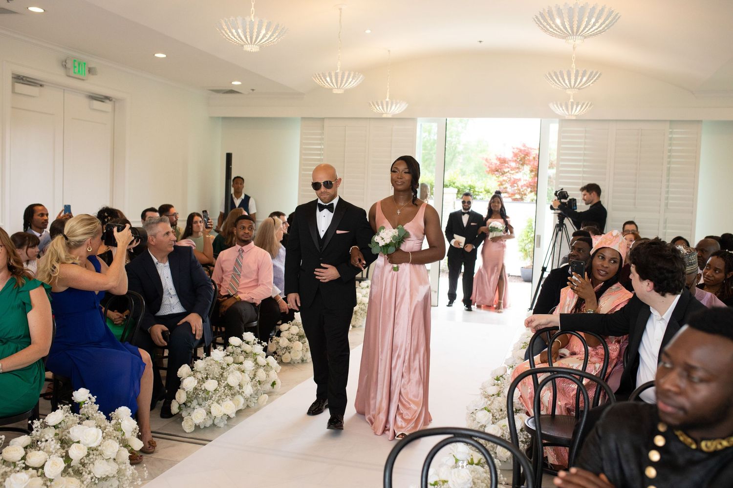Indoor wedding ceremony space with white decor and guests seated in rows.