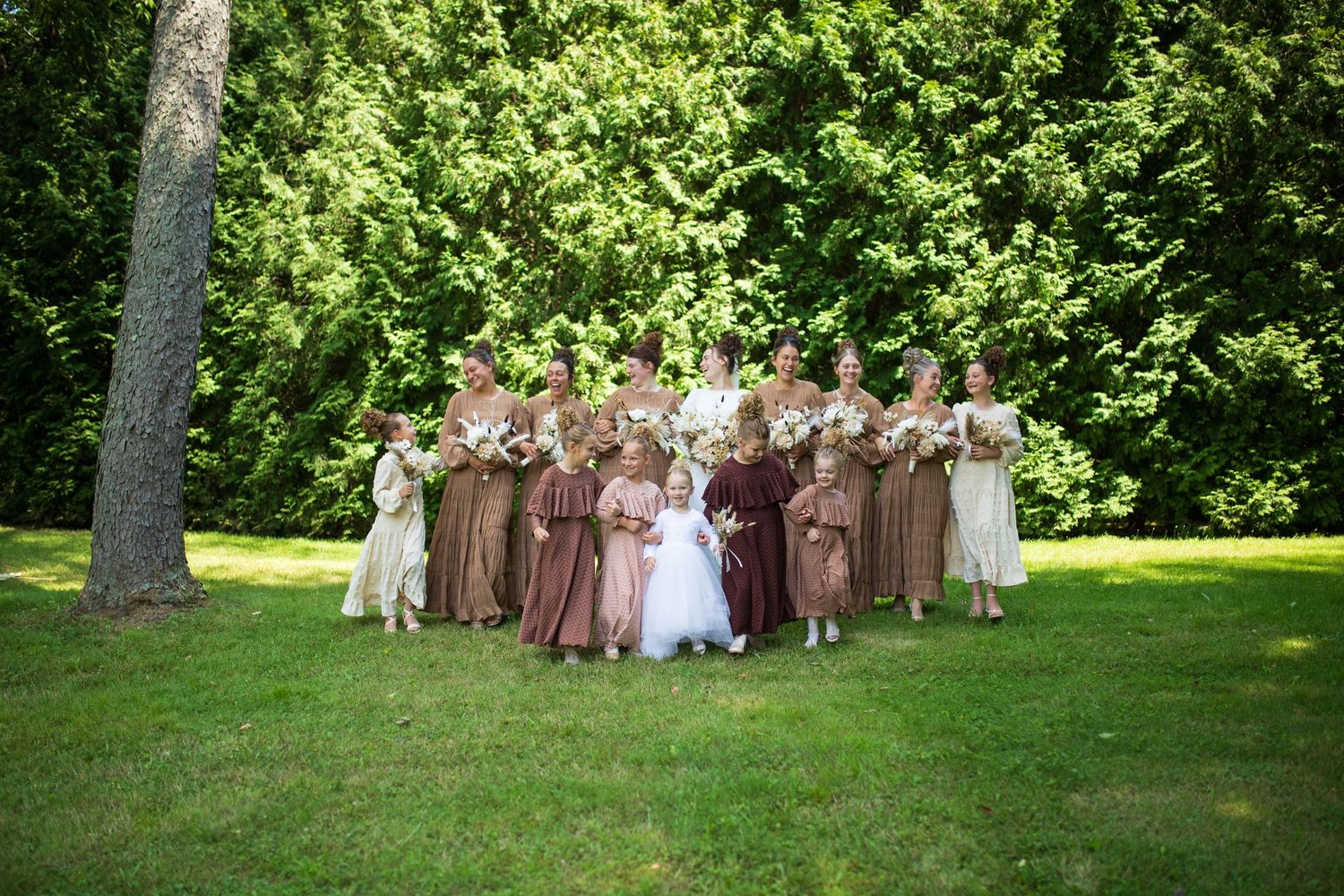 Wedding party forms a V-shape on green lawn wearing coordinating brown and cream dresses.