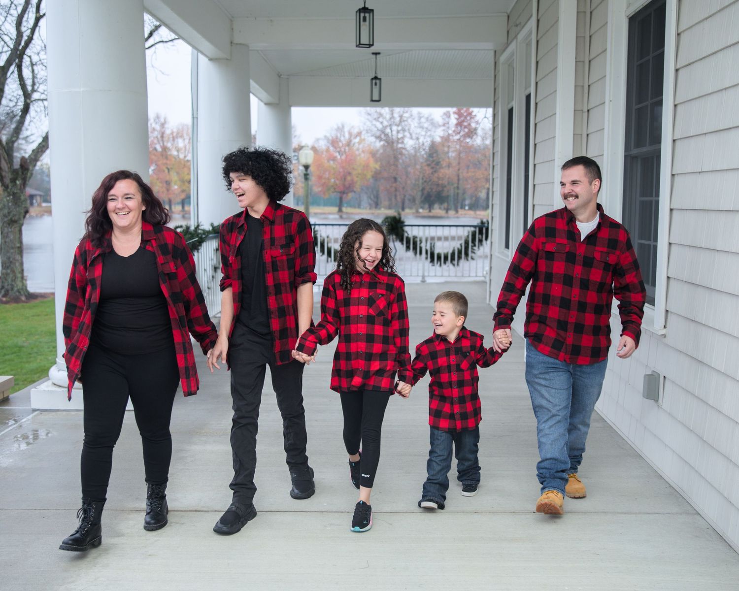 People in matching red and black buffalo plaid shirts walk along a white colonial porch.
