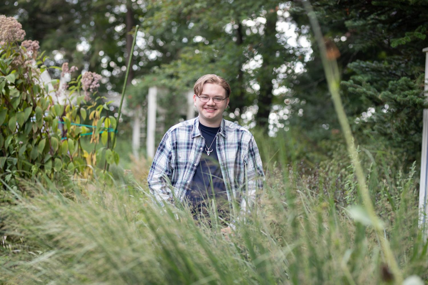 People stand casually among tall grass and wildflowers in a natural outdoor setting.