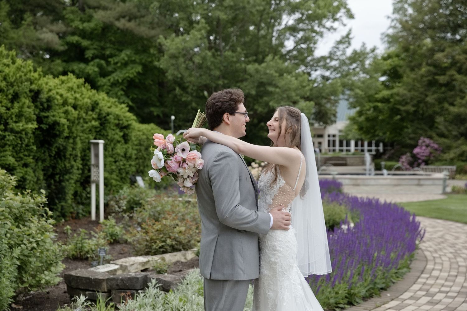 Bride and groom share a romantic embrace in a lush garden with purple lavender flowers in bloom.