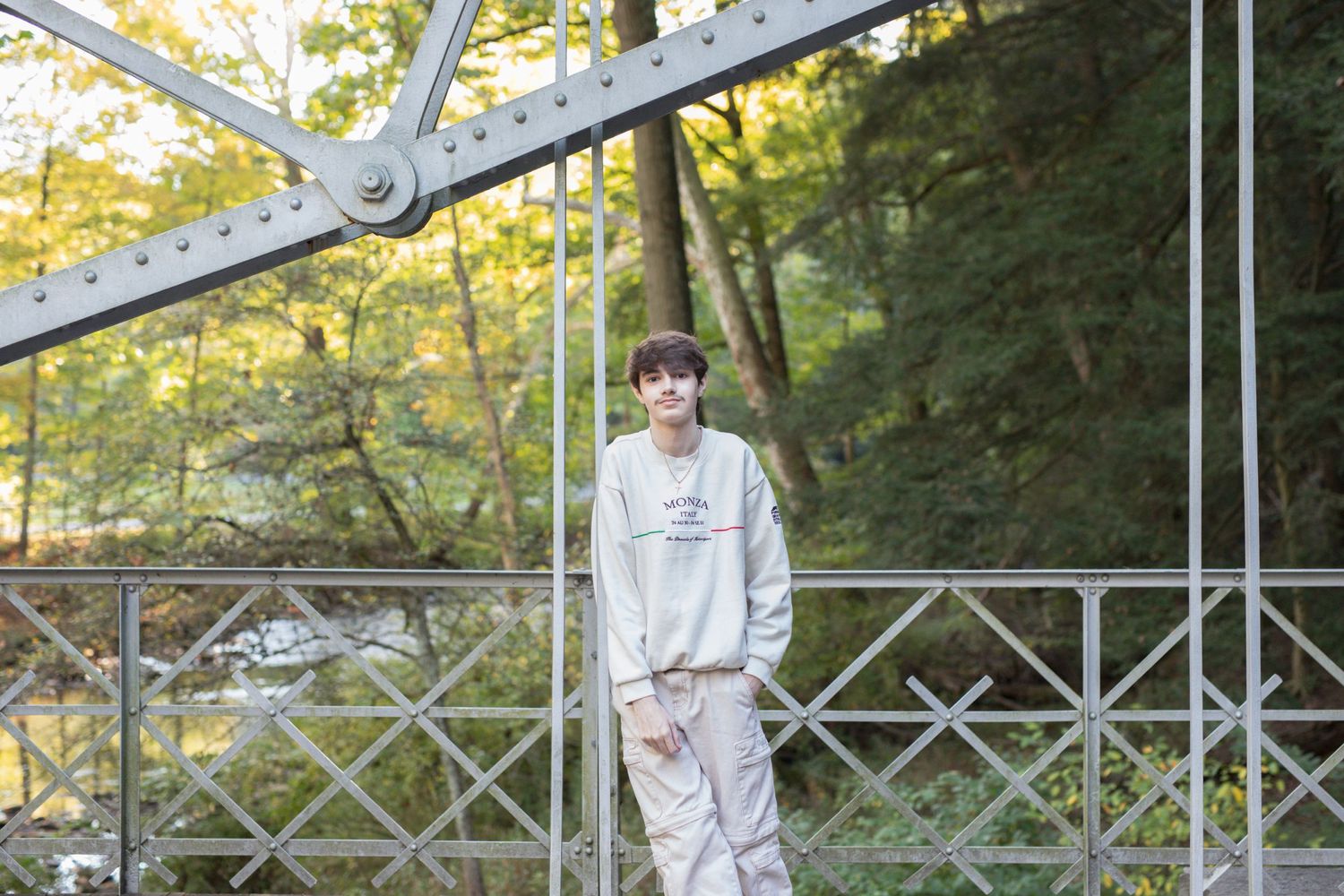 Person in light colored clothing poses against metal architectural framework outdoors.