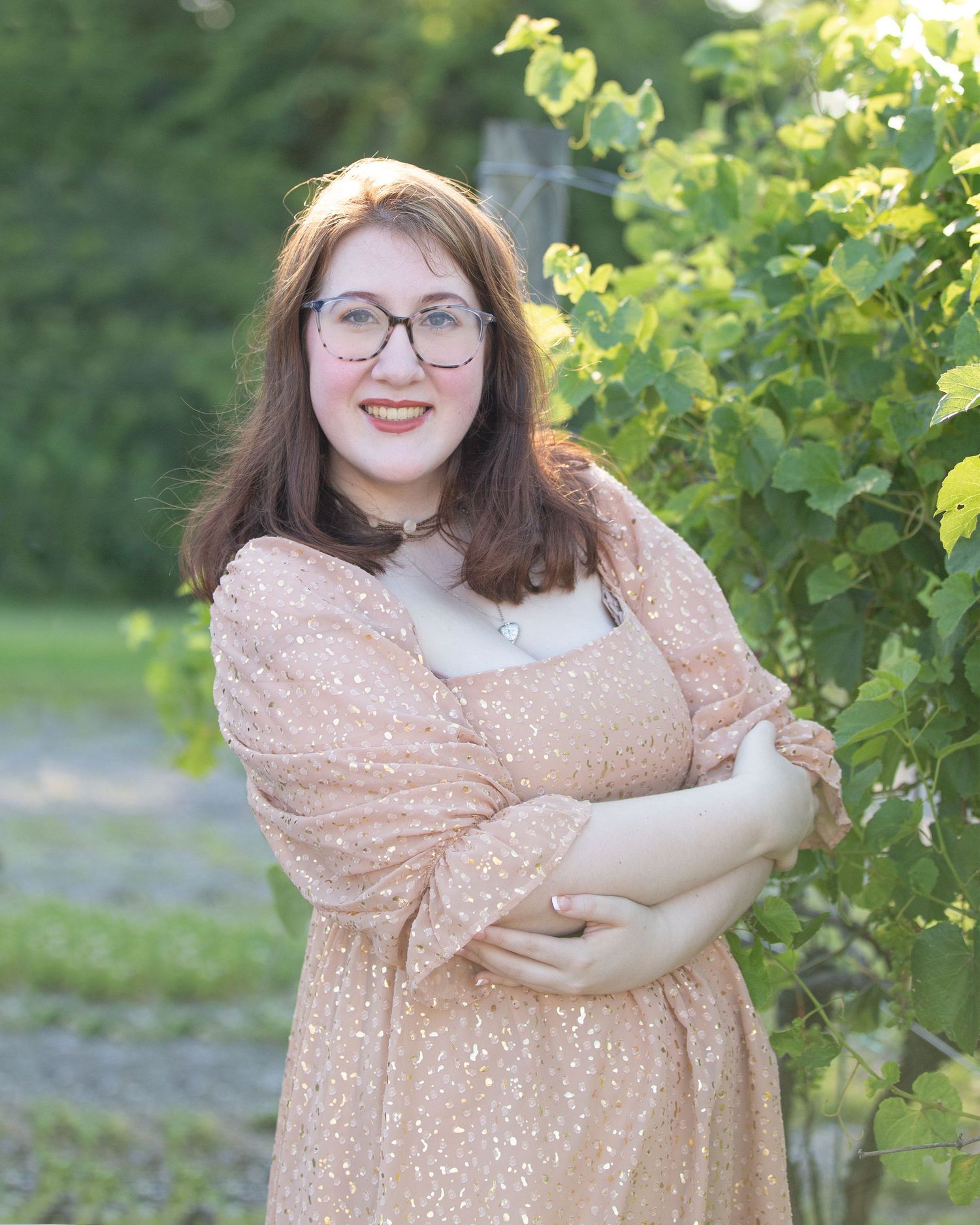 A woman in a sparkly peach dress poses in front of lush green foliage at sunset.