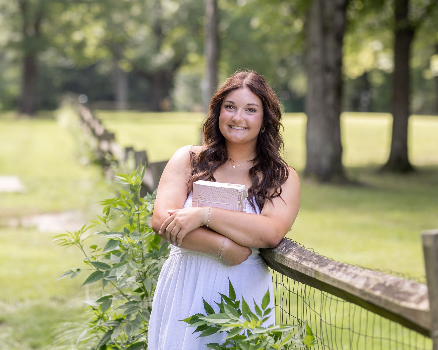 A casual summer portrait session in a park with a rustic wooden fence and natural greenery.