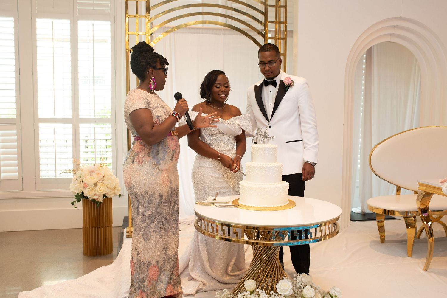 Joyful wedding cake cutting celebration in an elegant white reception venue.