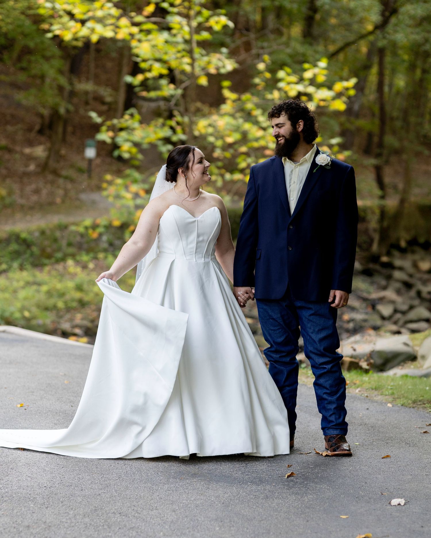 Bride in classic white gown walks with groom on autumn path.