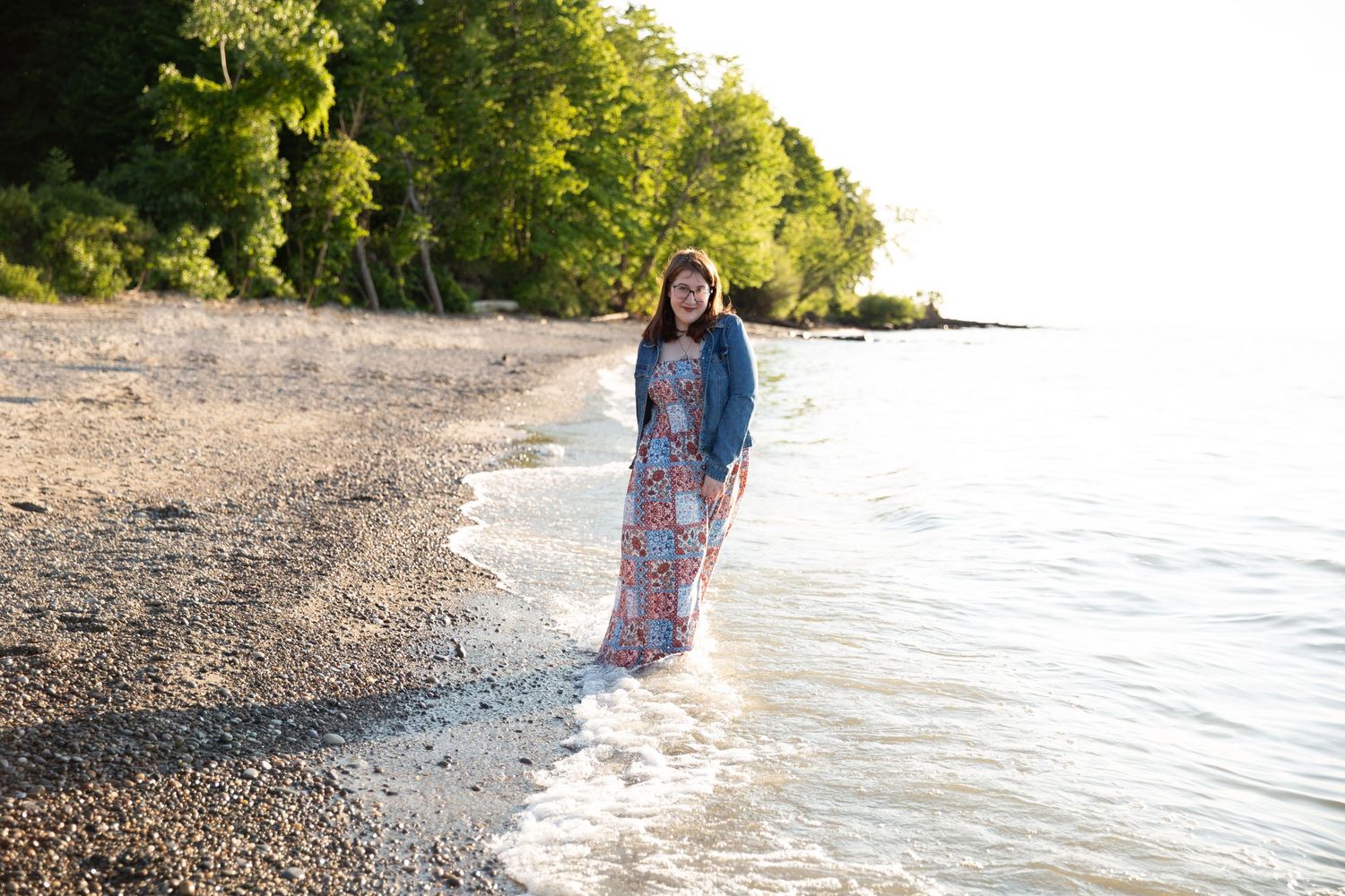 A woman in a floral dress walks along a peaceful beach shoreline at sunset.