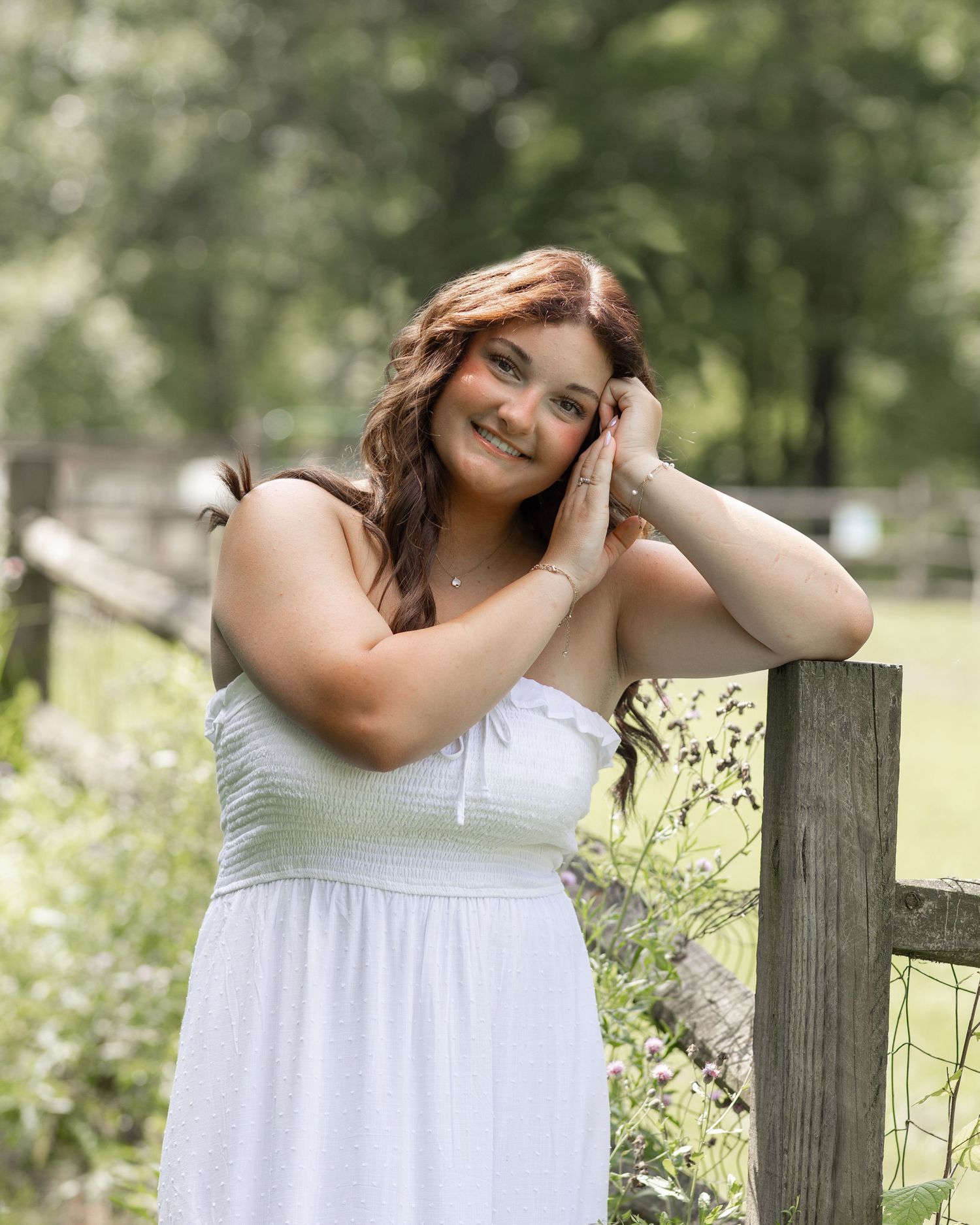 A dreamy summer portrait against a rustic fence with soft natural lighting.