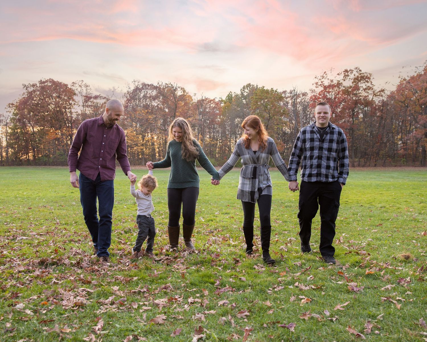 Family group walking together across an autumn field at sunset.